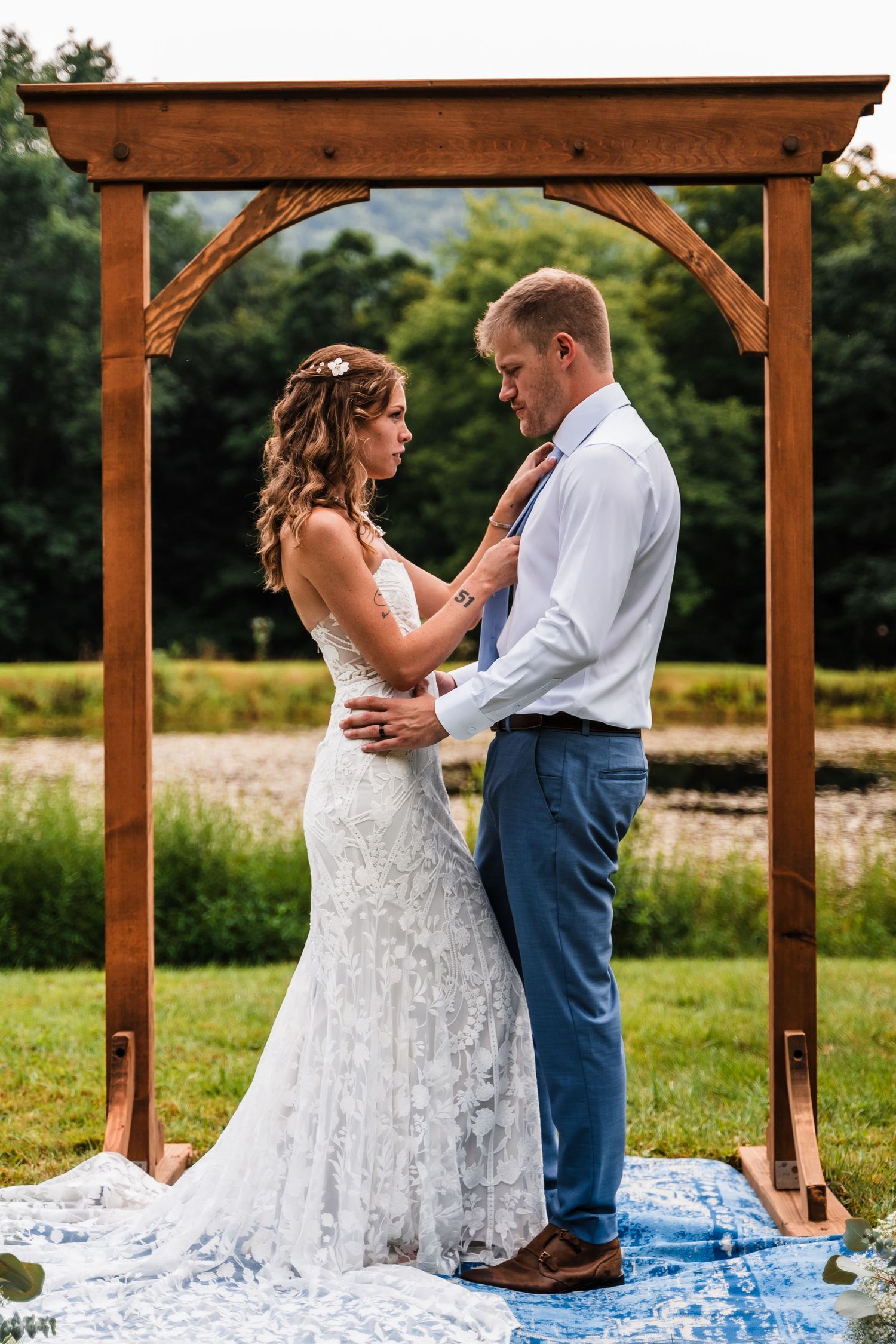 A tender moment between newlyweds under a wooden wedding arch with a blue runner.