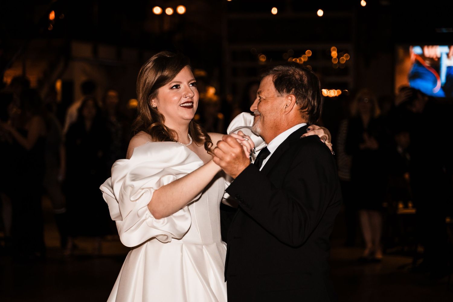 Couple sharing dance together during evening wedding reception with warm lighting.