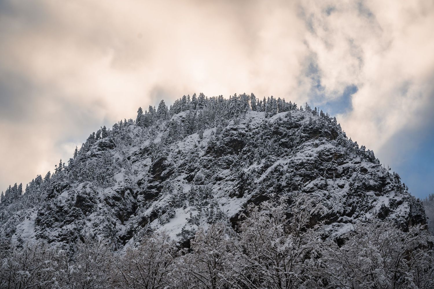 Snow-covered mountain peaks rise against a cloudy sky in a dramatic winter landscape.