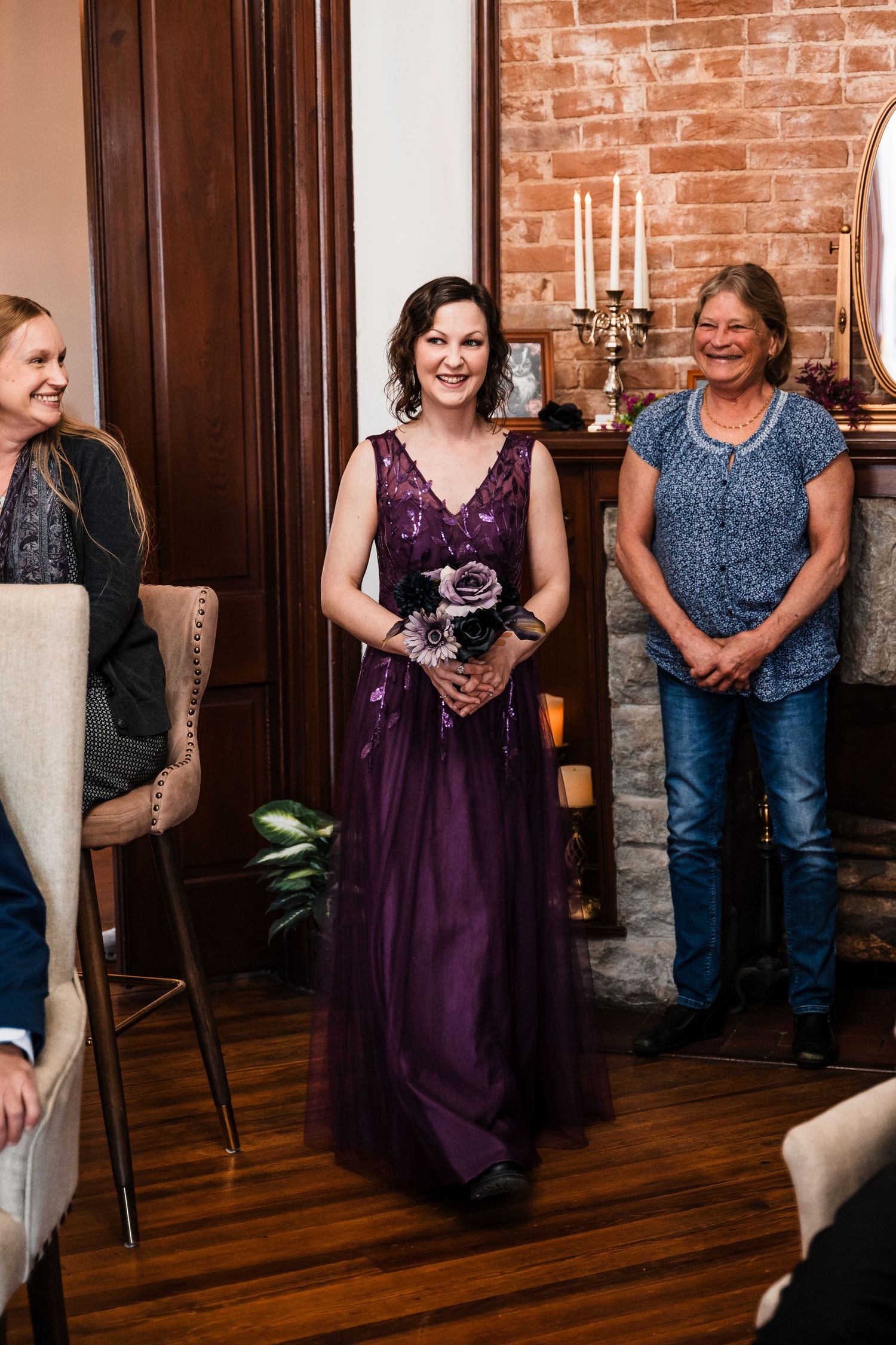 Bridesmaid in elegant purple gown holding bouquet walks down aisle at indoor wedding ceremony.