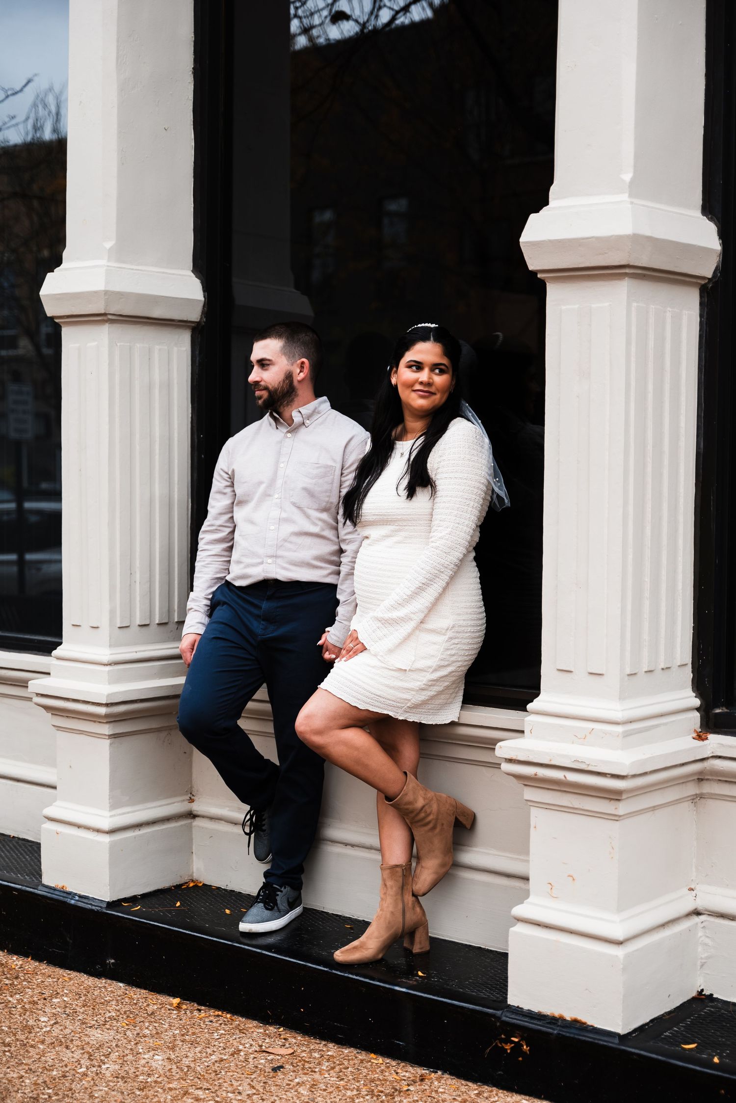 A couple poses casually against white columns of a building's entrance.
