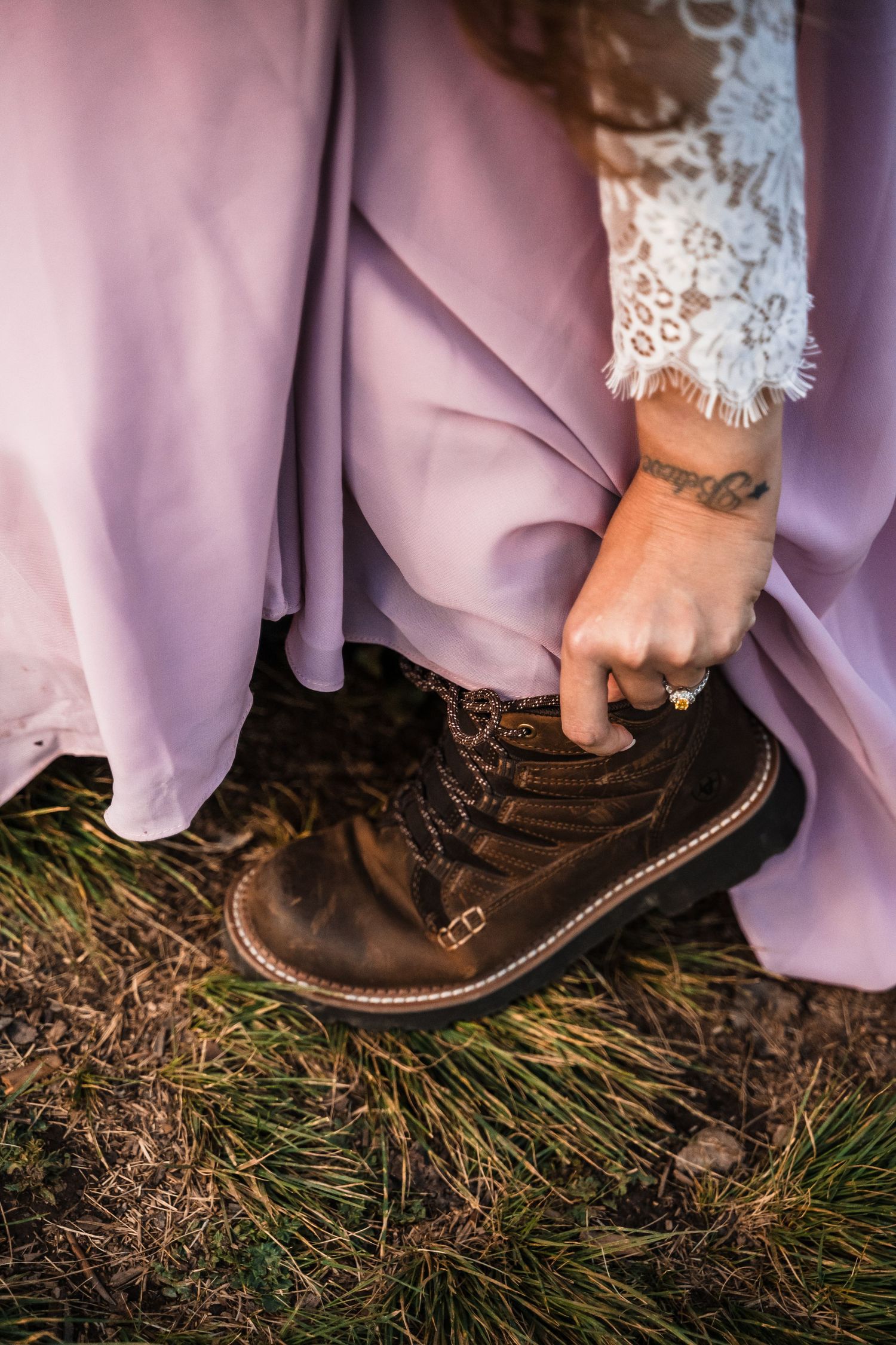 A close-up of hiking boots and a flowing pink dress against natural grass terrain.