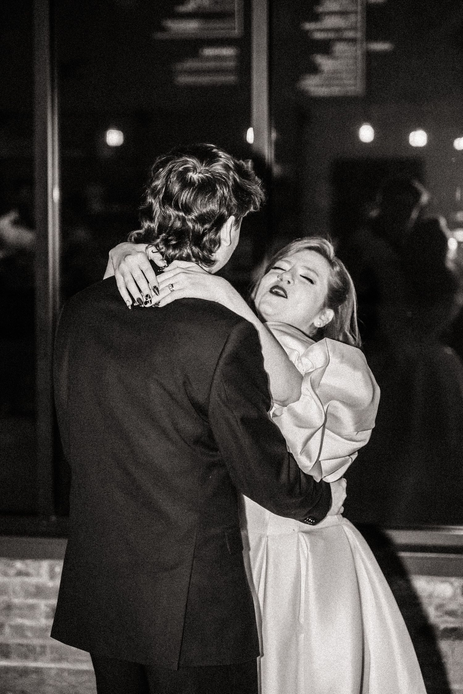 A black and white photo of a couple sharing a romantic dance moment in formal attire.