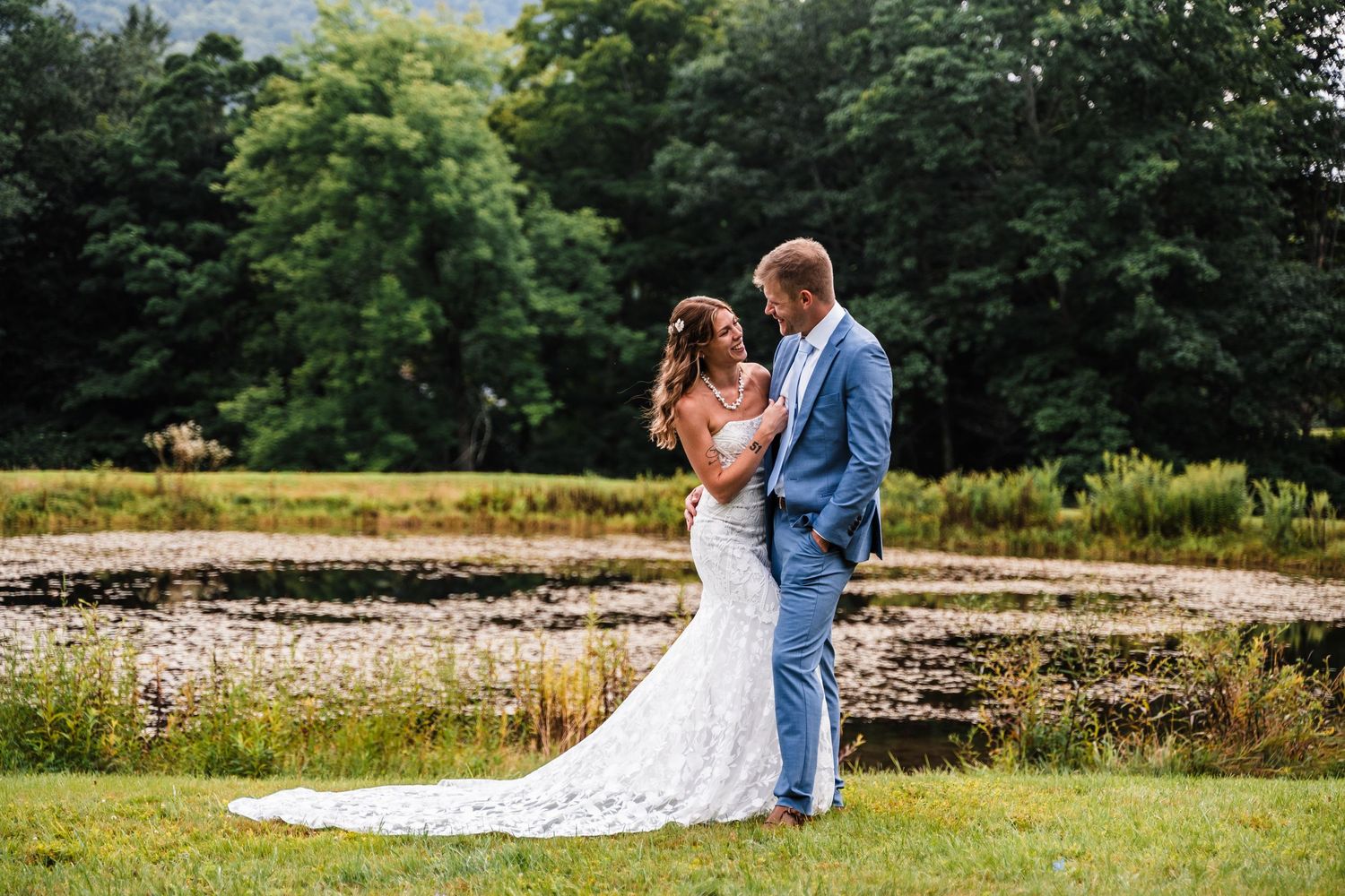 A romantic moment captured at an outdoor wedding with a natural pond and trees in the background.