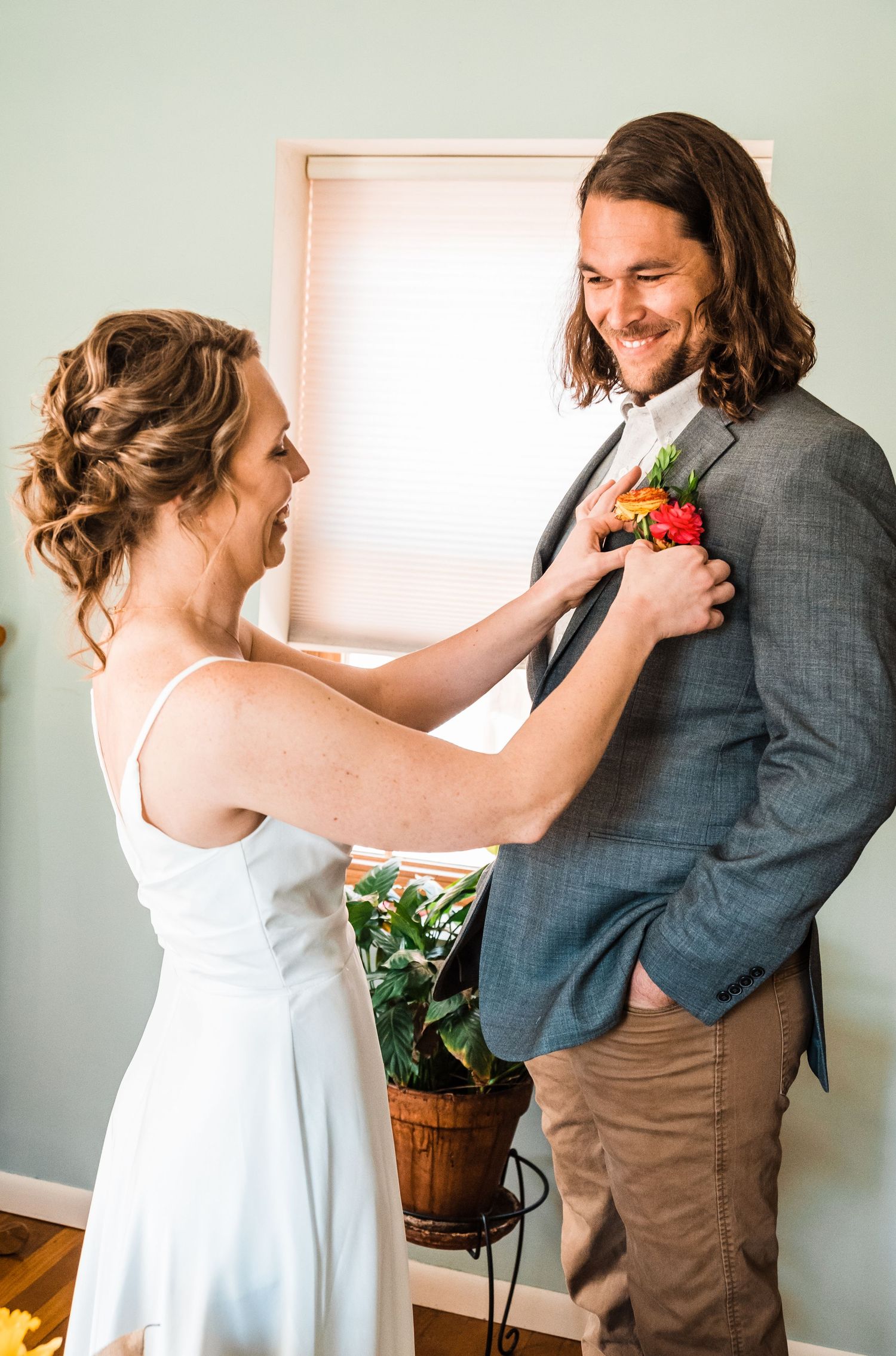 A couple sharing a joyful moment while adjusting flowers on a grey suit jacket.