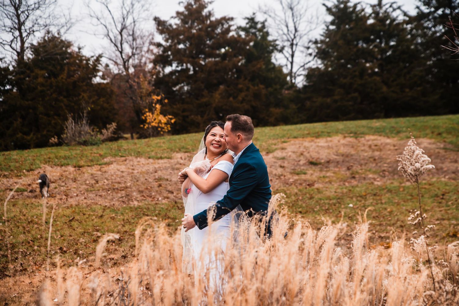 Romantic moment captured in golden field with autumn trees in background.