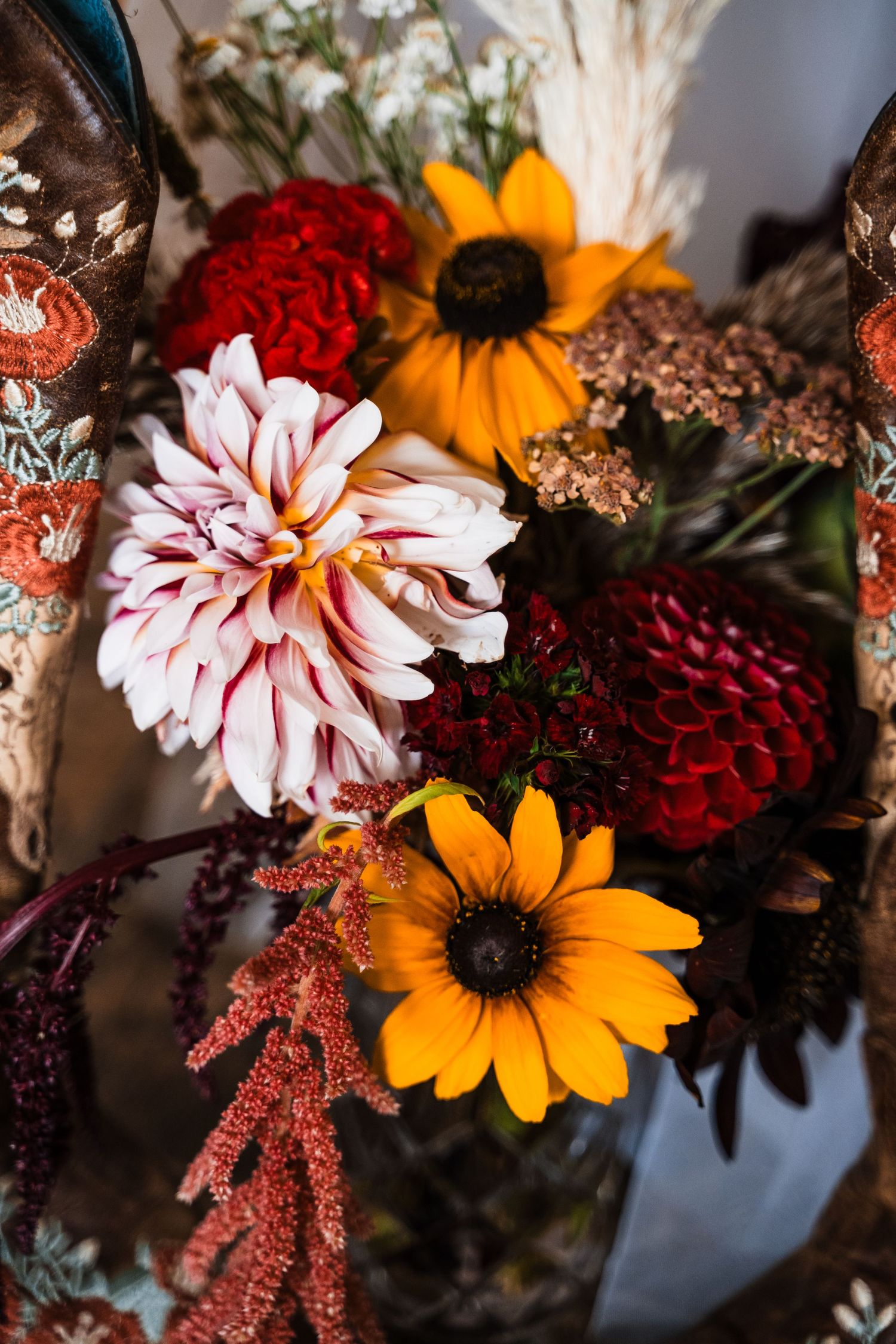 A vibrant fall flower arrangement featuring sunflowers, pink and red dahlias, and rusty autumn foliage in warm lighting.