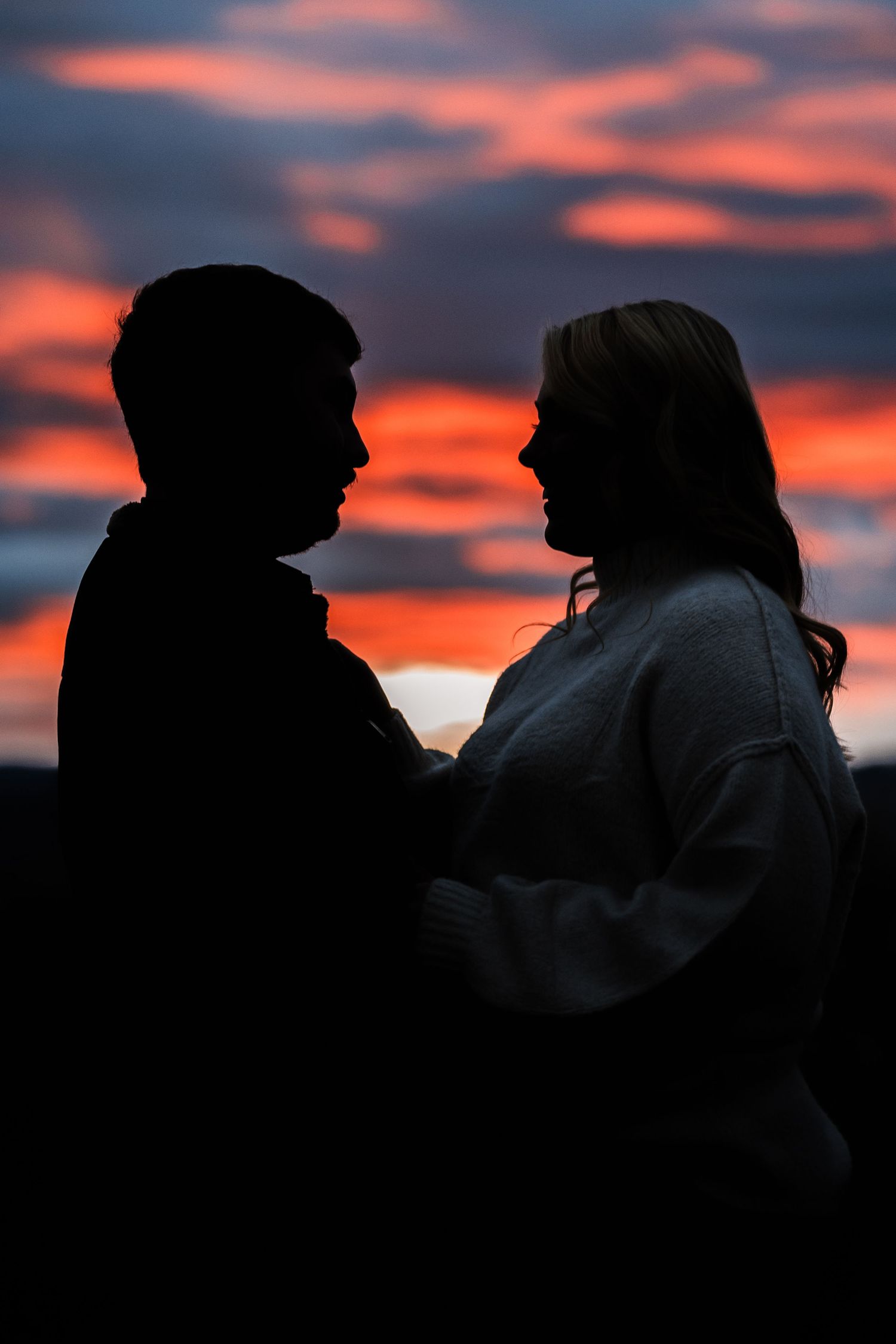 Two silhouettes embrace against a dramatic orange and purple sunset sky.