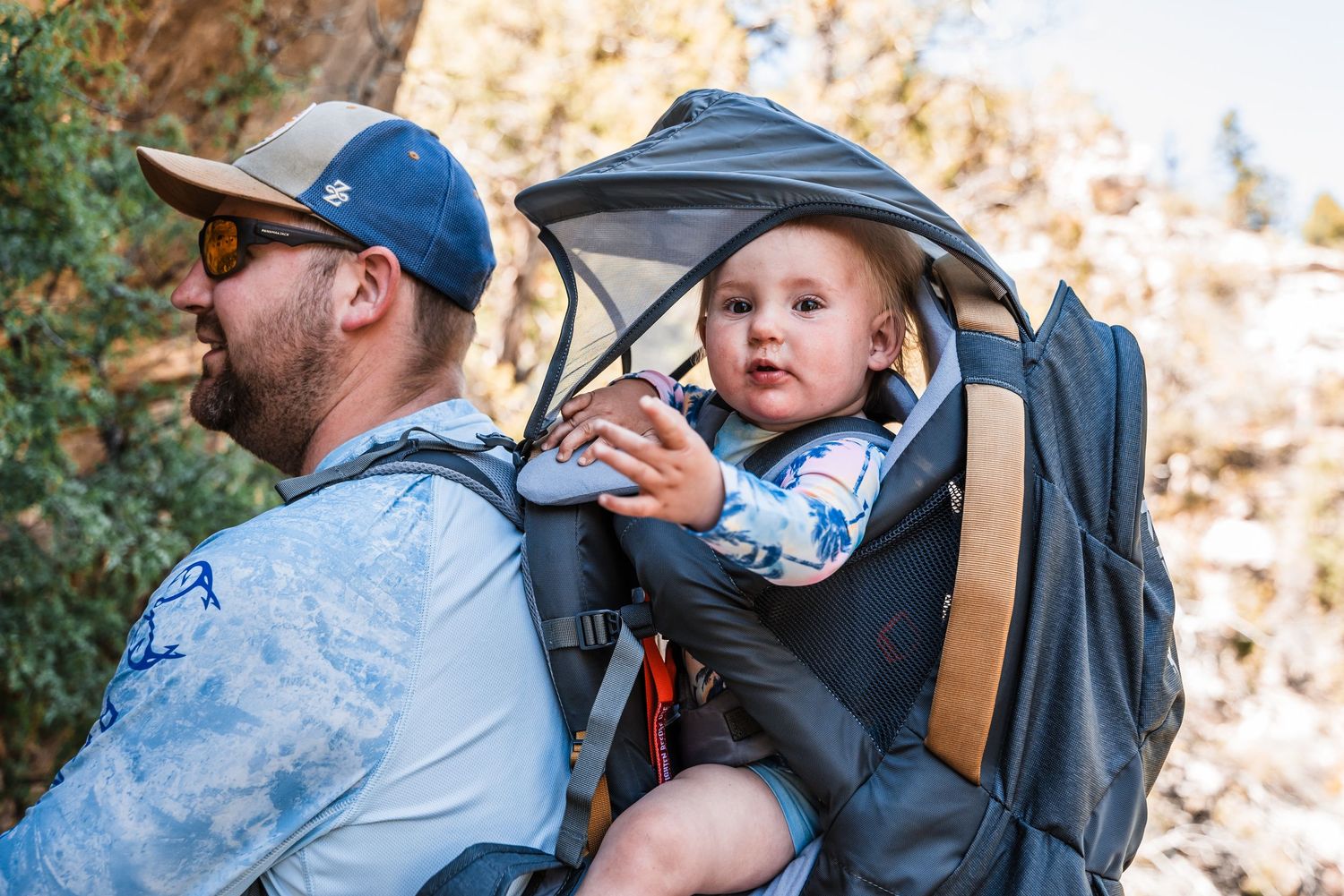 A baby rides along in a black hiking carrier backpack during an outdoor adventure.
