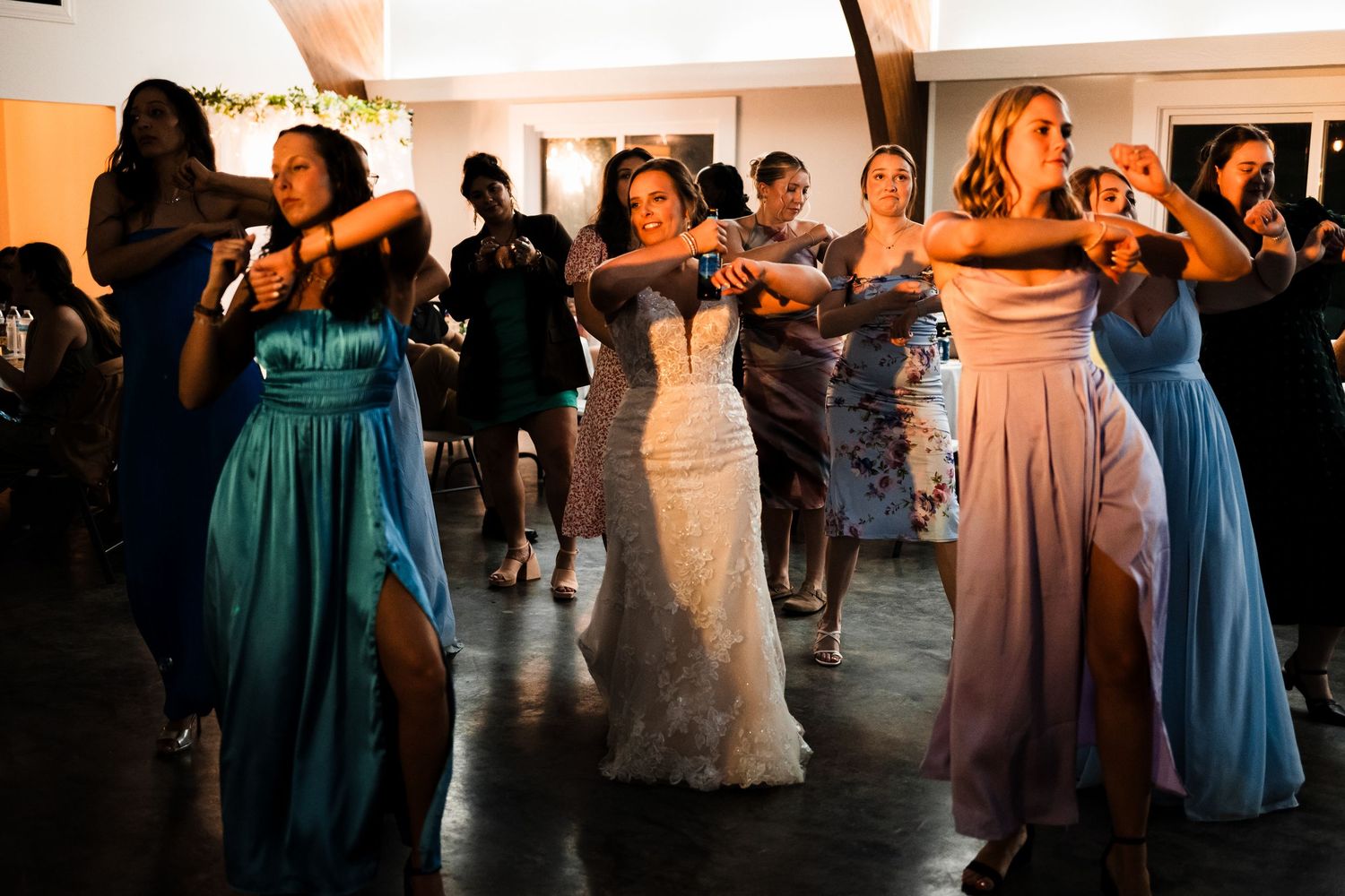 Wedding party dancing in colorful formal dresses during reception celebration.