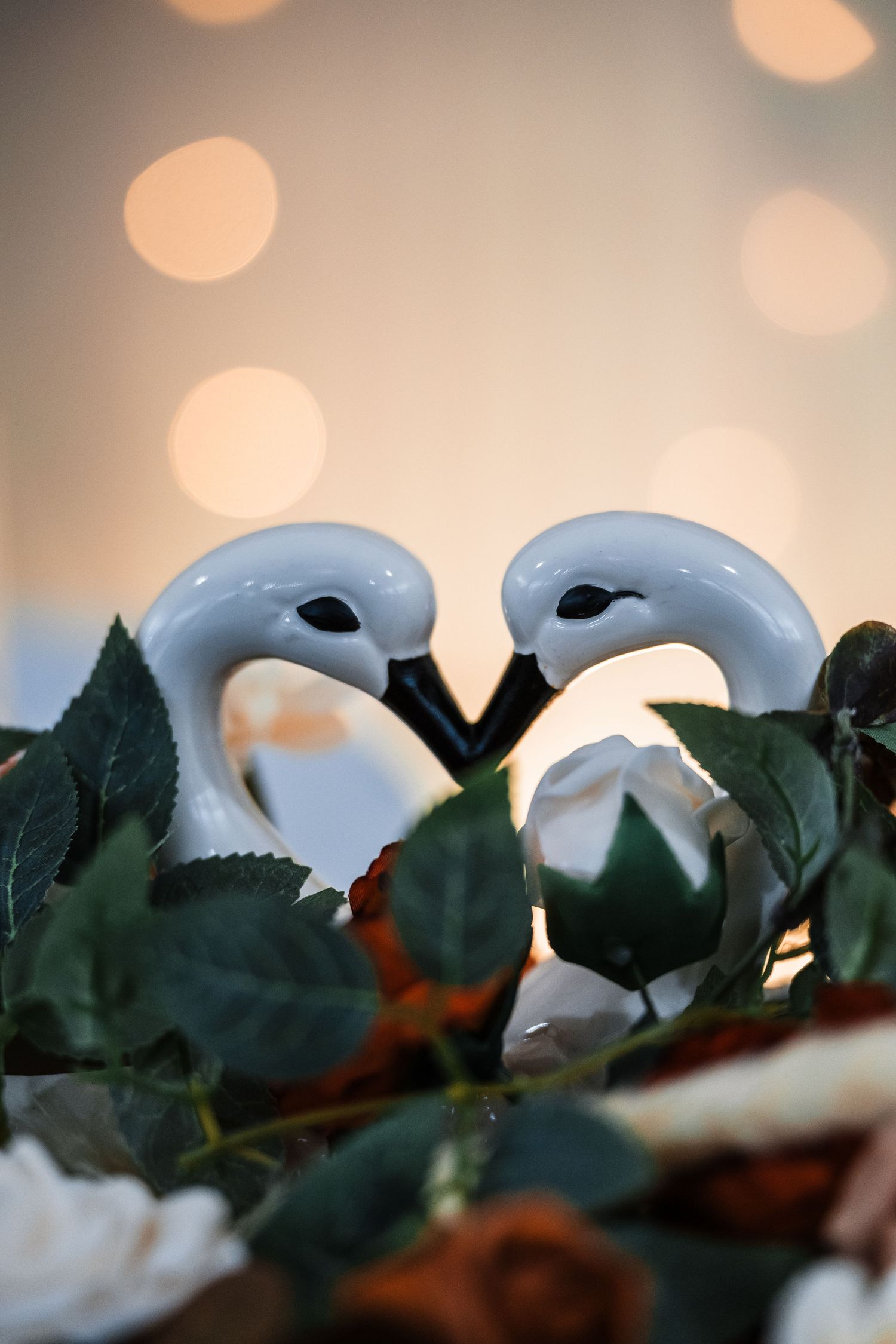 White decorative masks nestled among green leaves with soft bokeh lights in the background.