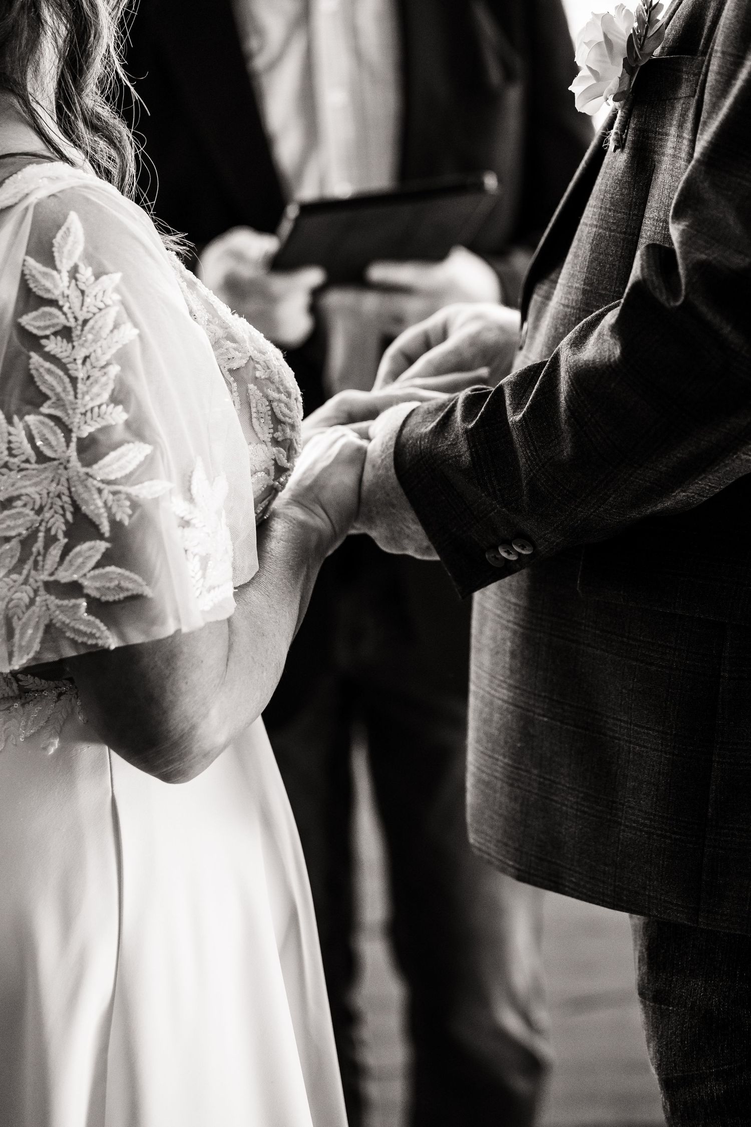 A black and white wedding photo showing details of a bride's lace dress sleeve next to a dark suit.