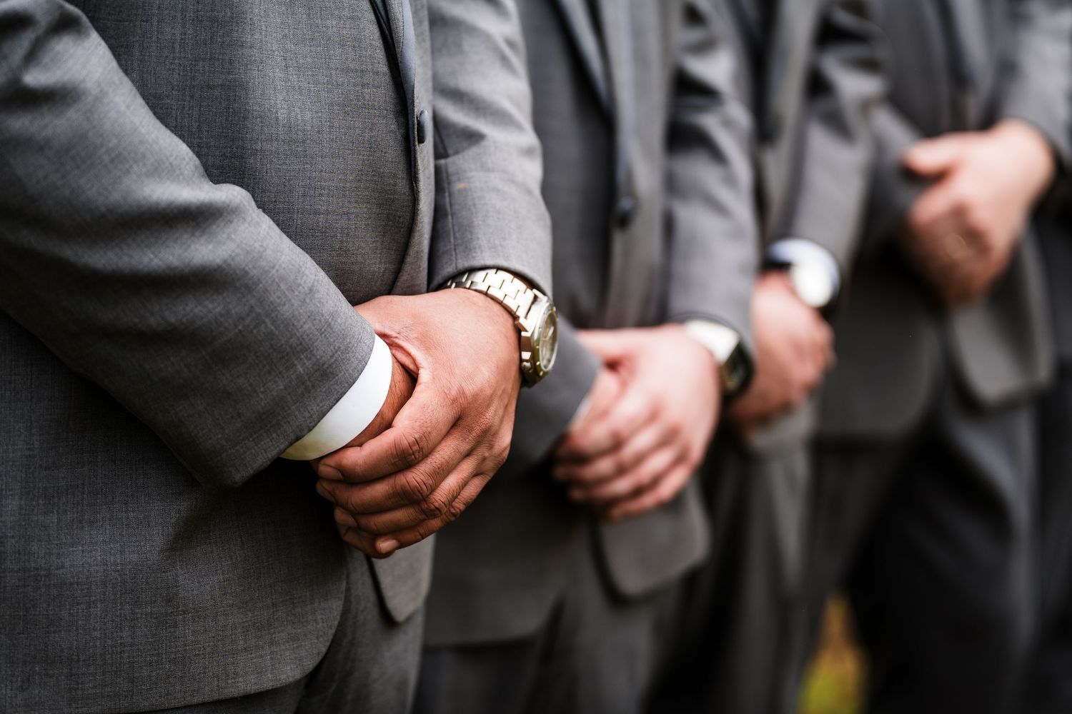 A row of men in gray suits standing with hands clasped in front of them at formal event.