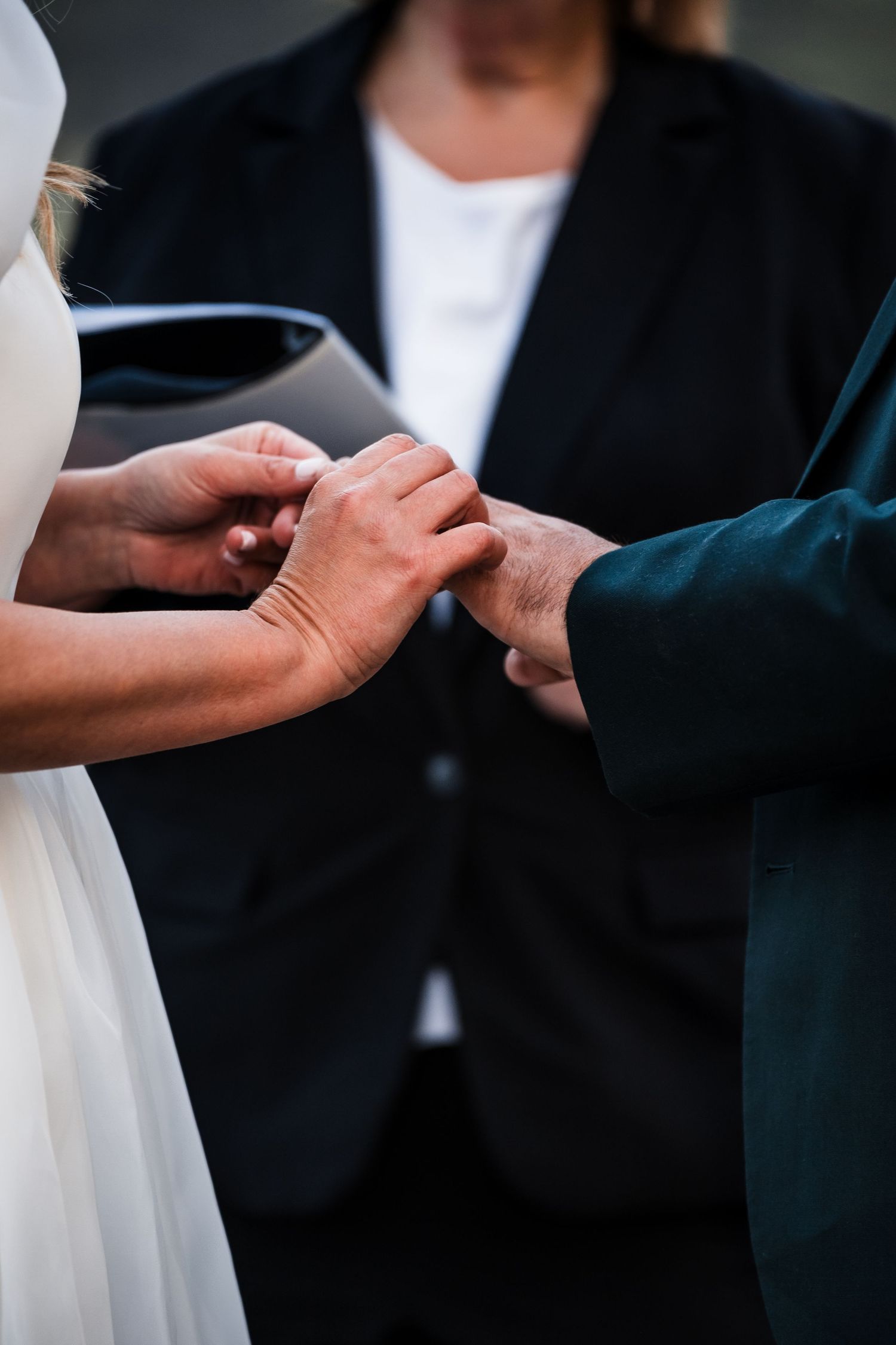 Close-up shot of hands exchanging rings during an outdoor wedding ceremony.