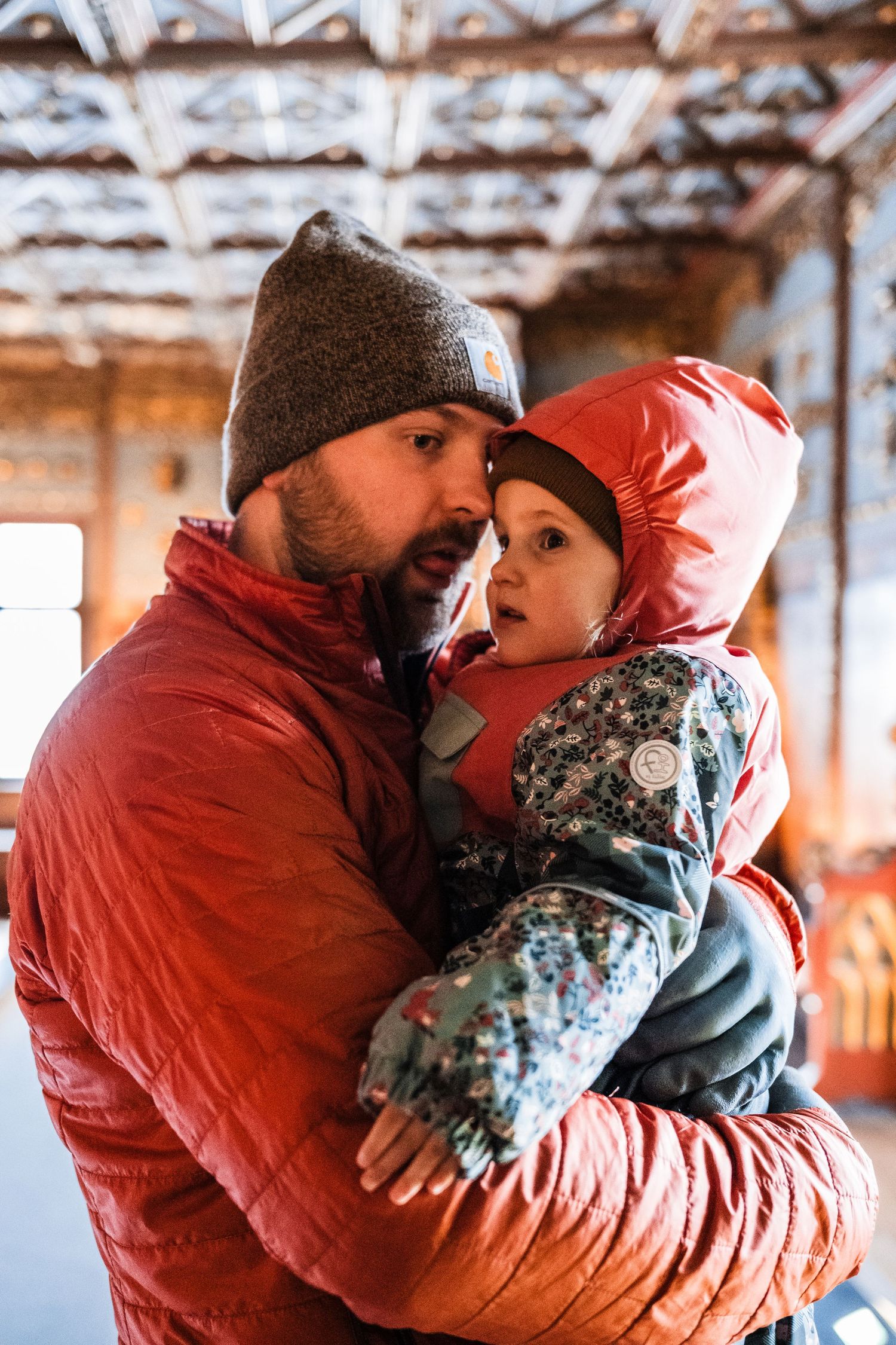 Two people in winter coats share an intimate moment in a rustic indoor setting.