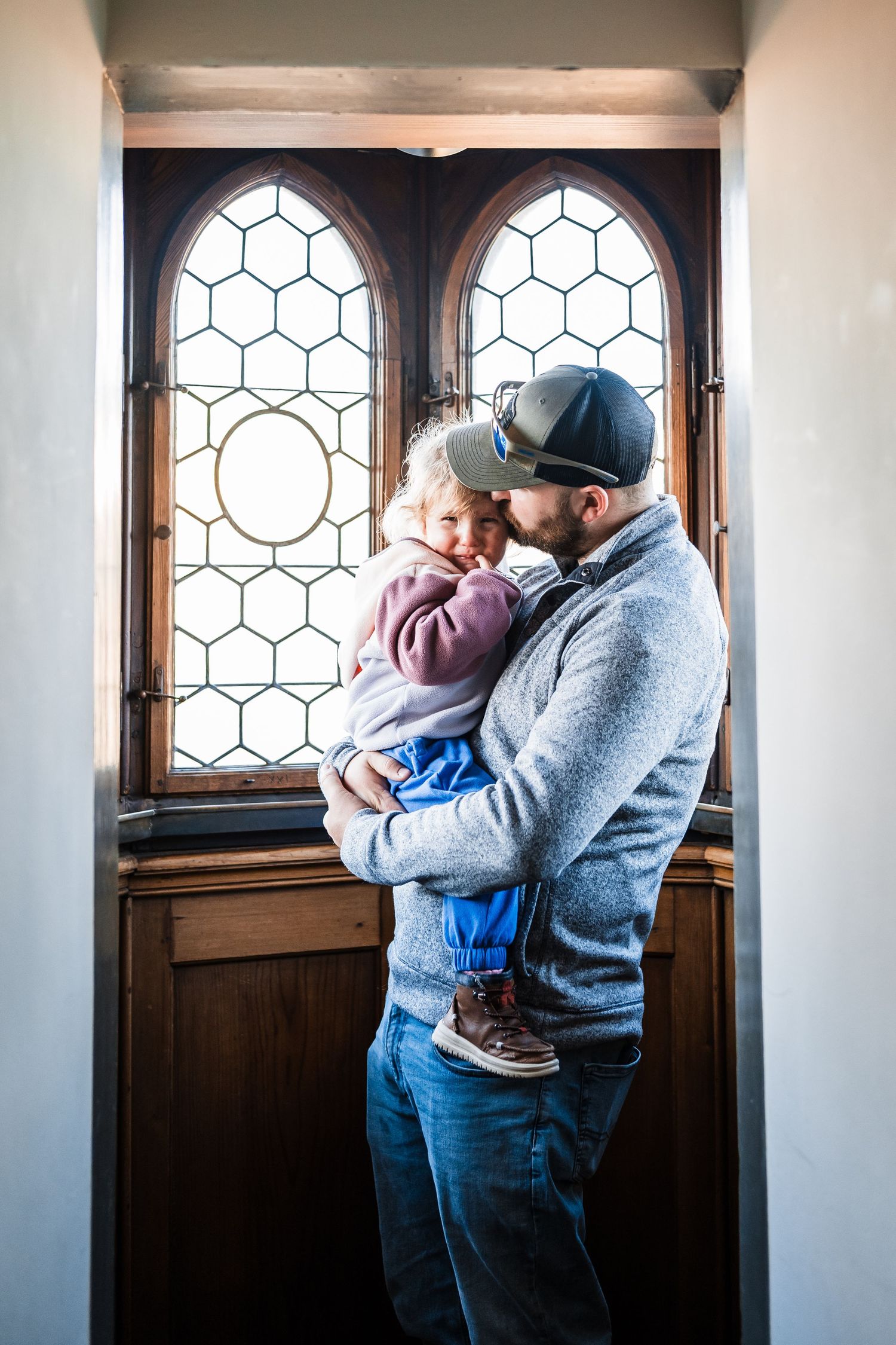 A parent holds a small baby by a decorative window in a series of three connected photos.