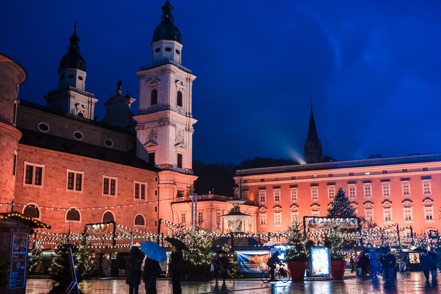 Historic European cathedral and buildings lit up at night with a deep blue twilight sky.