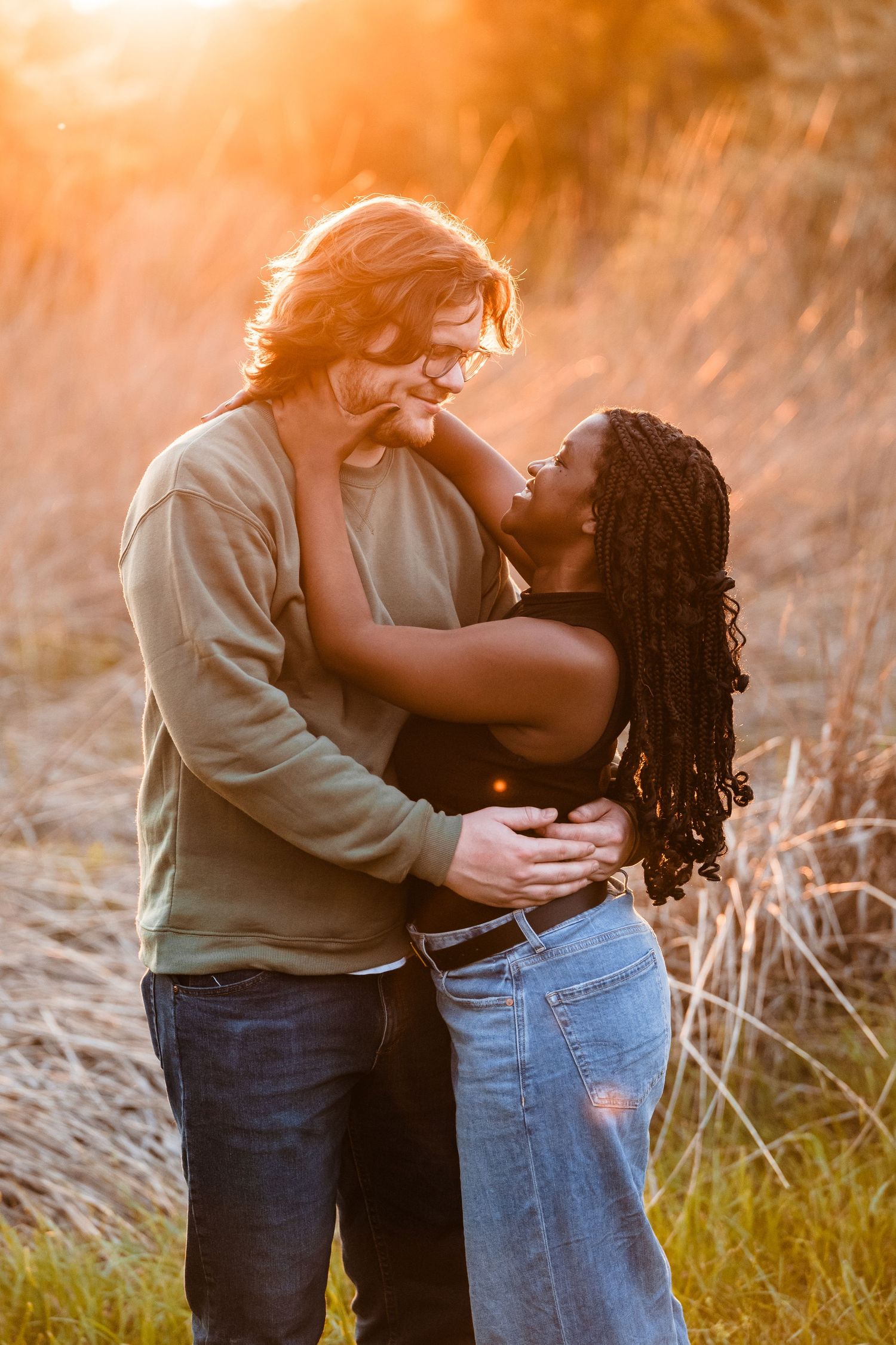 A romantic couple embraces in a field at golden hour with sunlit grass in the background.