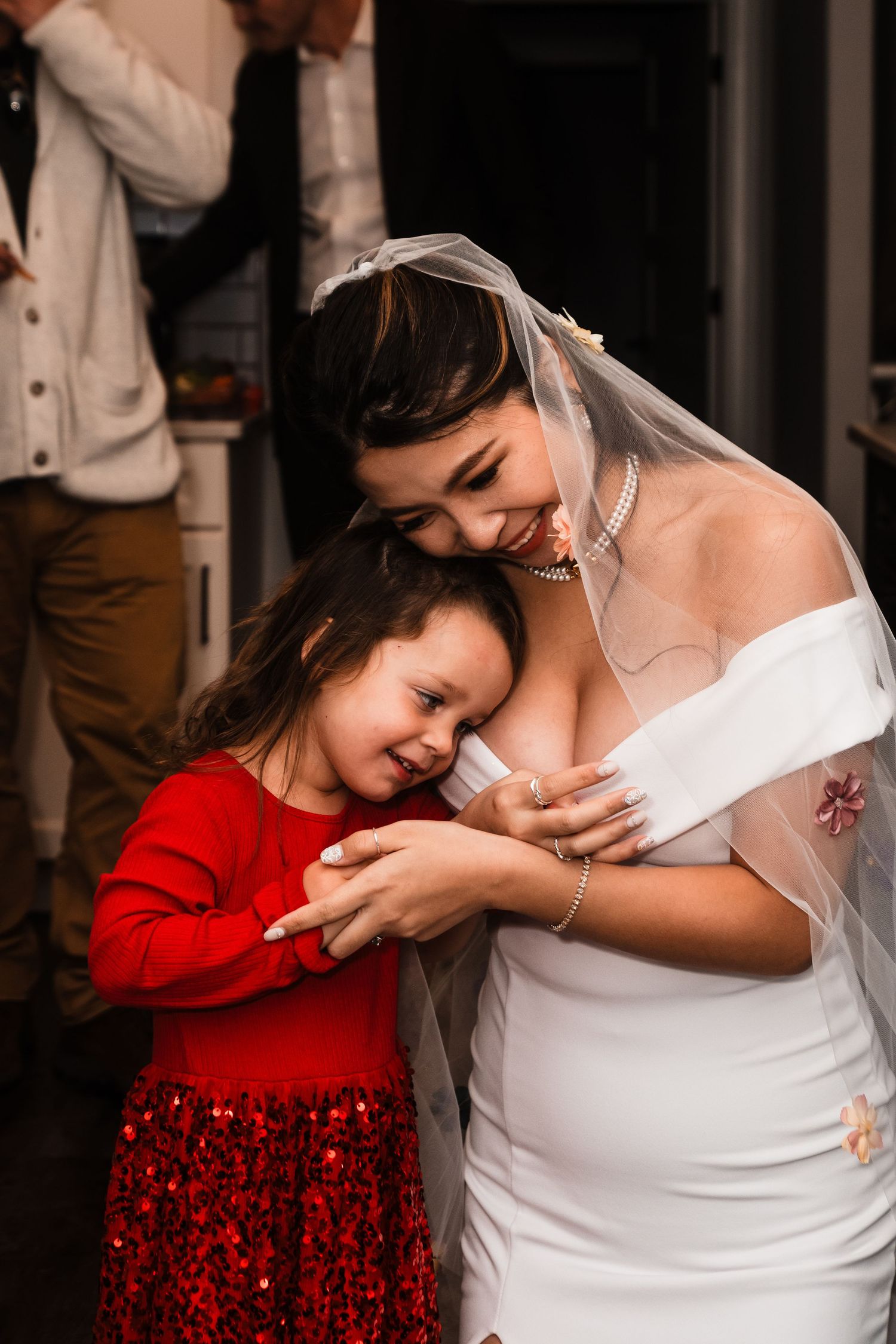 A tender moment shared between a bride in white and a child in a sparkly red dress.