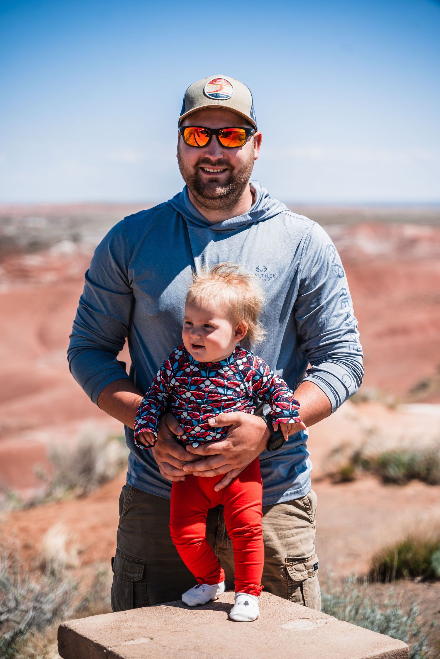 Parent and child stand together against a scenic desert landscape backdrop with blue sky.