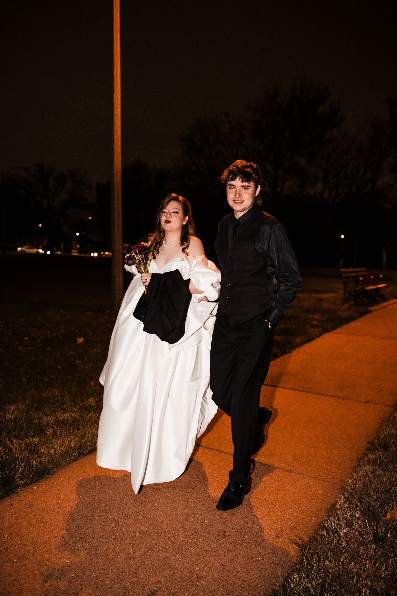 Couple walks together on illuminated pathway during nighttime wedding celebration.