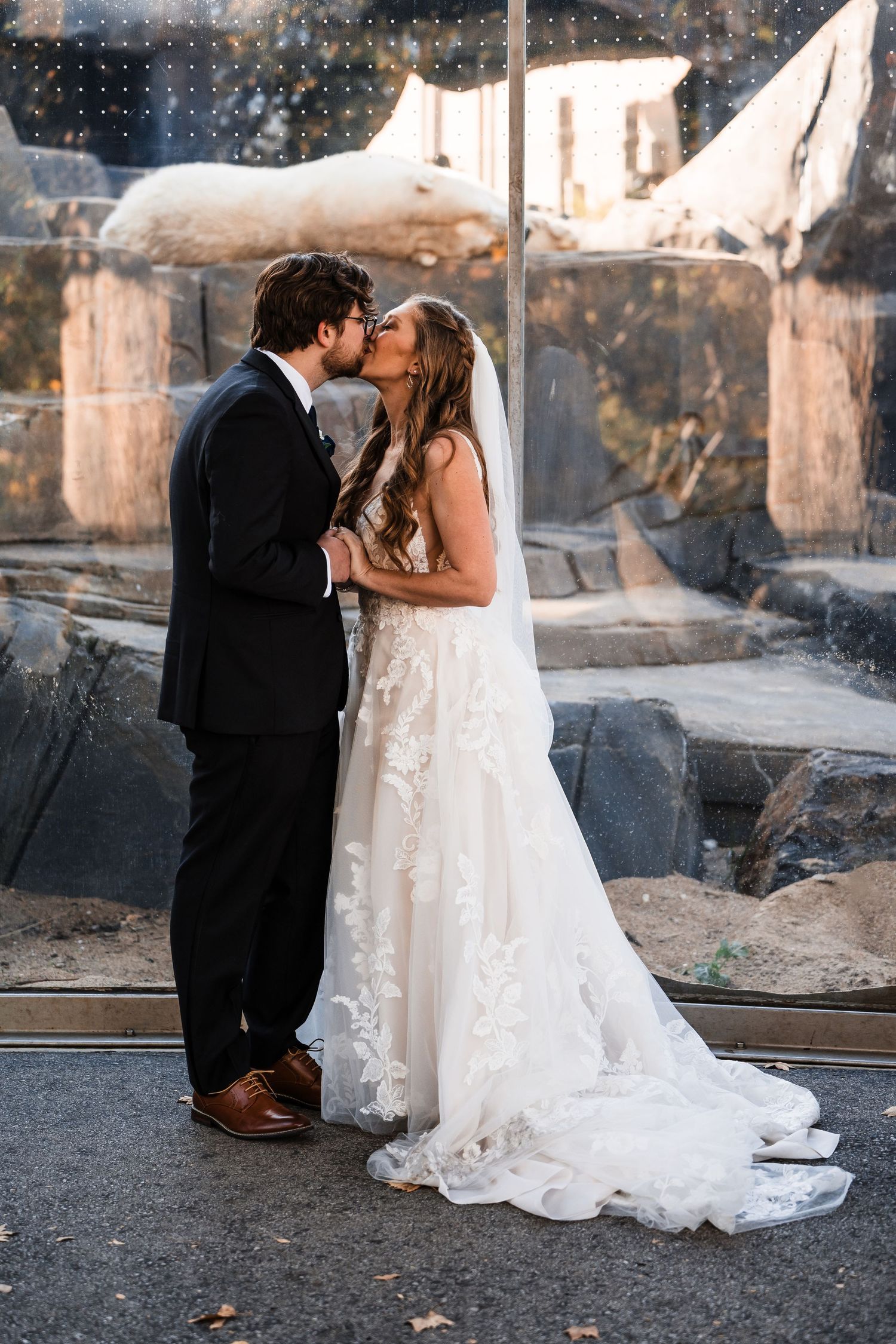 Couple kisses in elegant wedding attire against modern architectural backdrop.