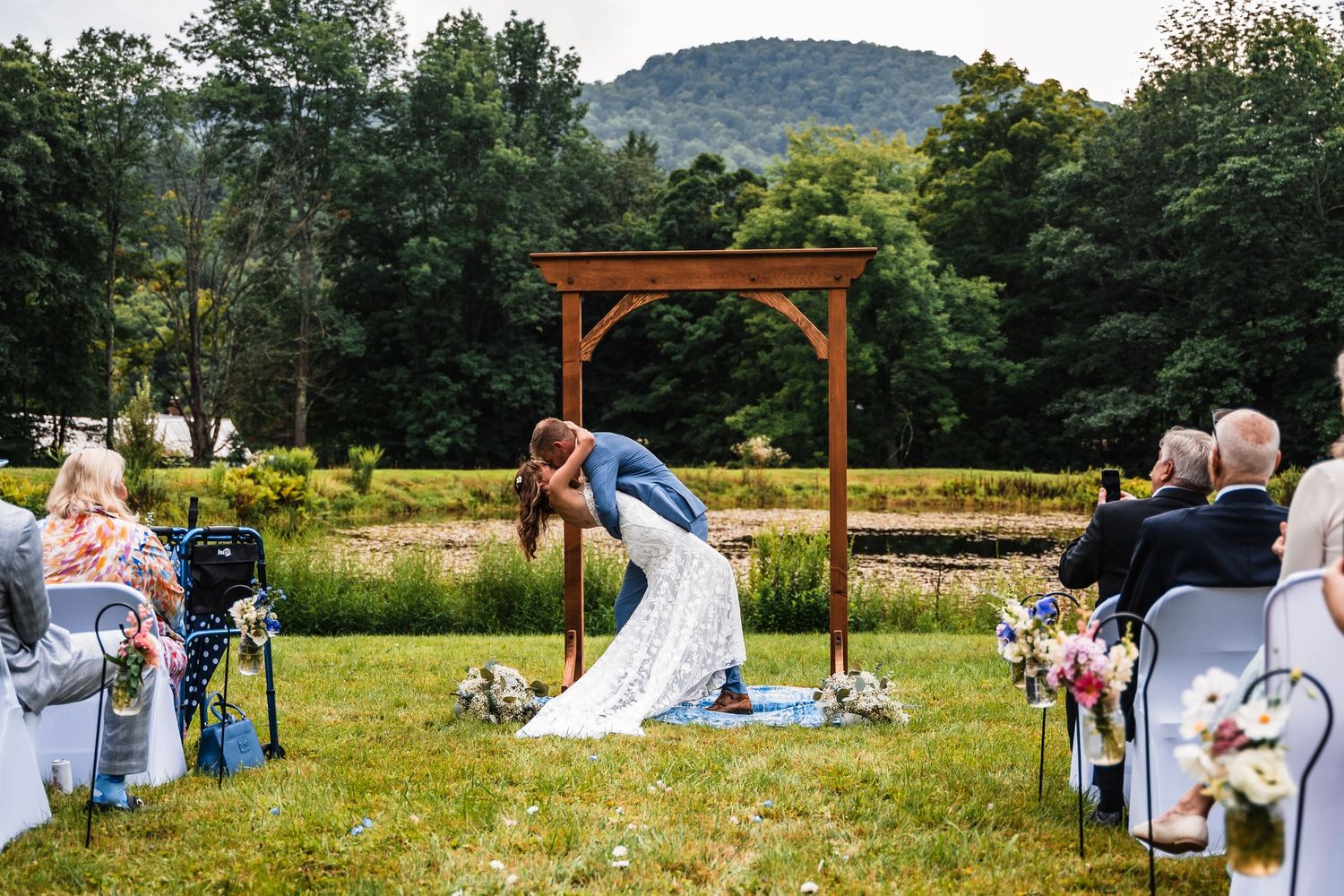 Romantic moment captured during outdoor wedding ceremony under wooden pergola with mountain views.