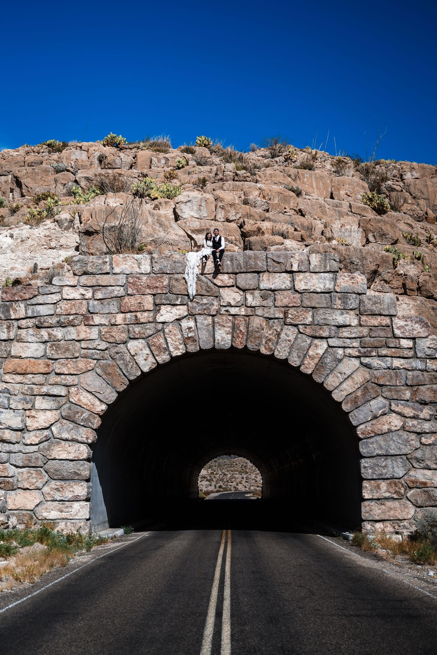 Stone arch tunnel entrance on a desert road with blue sky overhead.