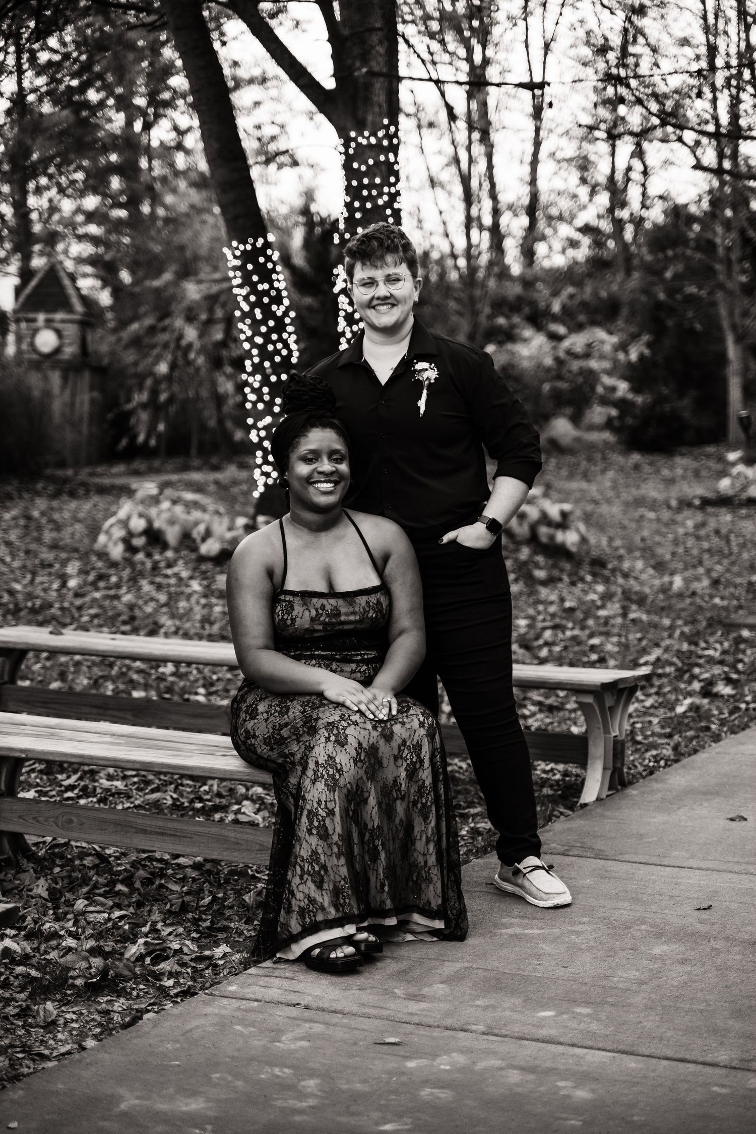 A black and white portrait on a garden bench with string lights twinkling in background.