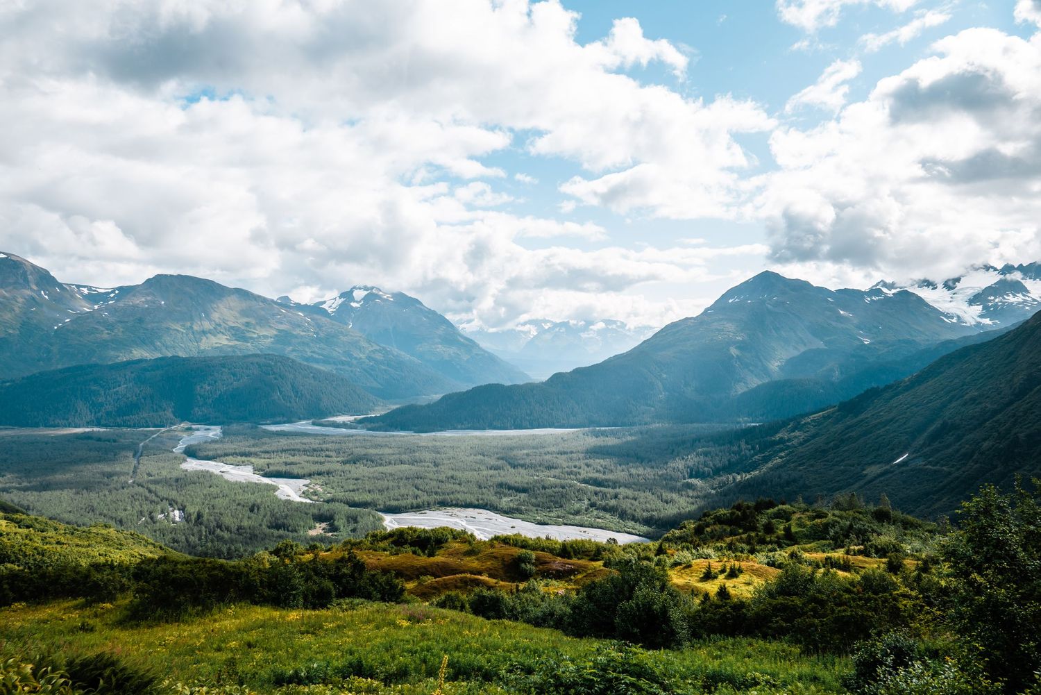 Scenic mountain valley landscape with winding river and green slopes under cloudy skies in remote wilderness terrain.