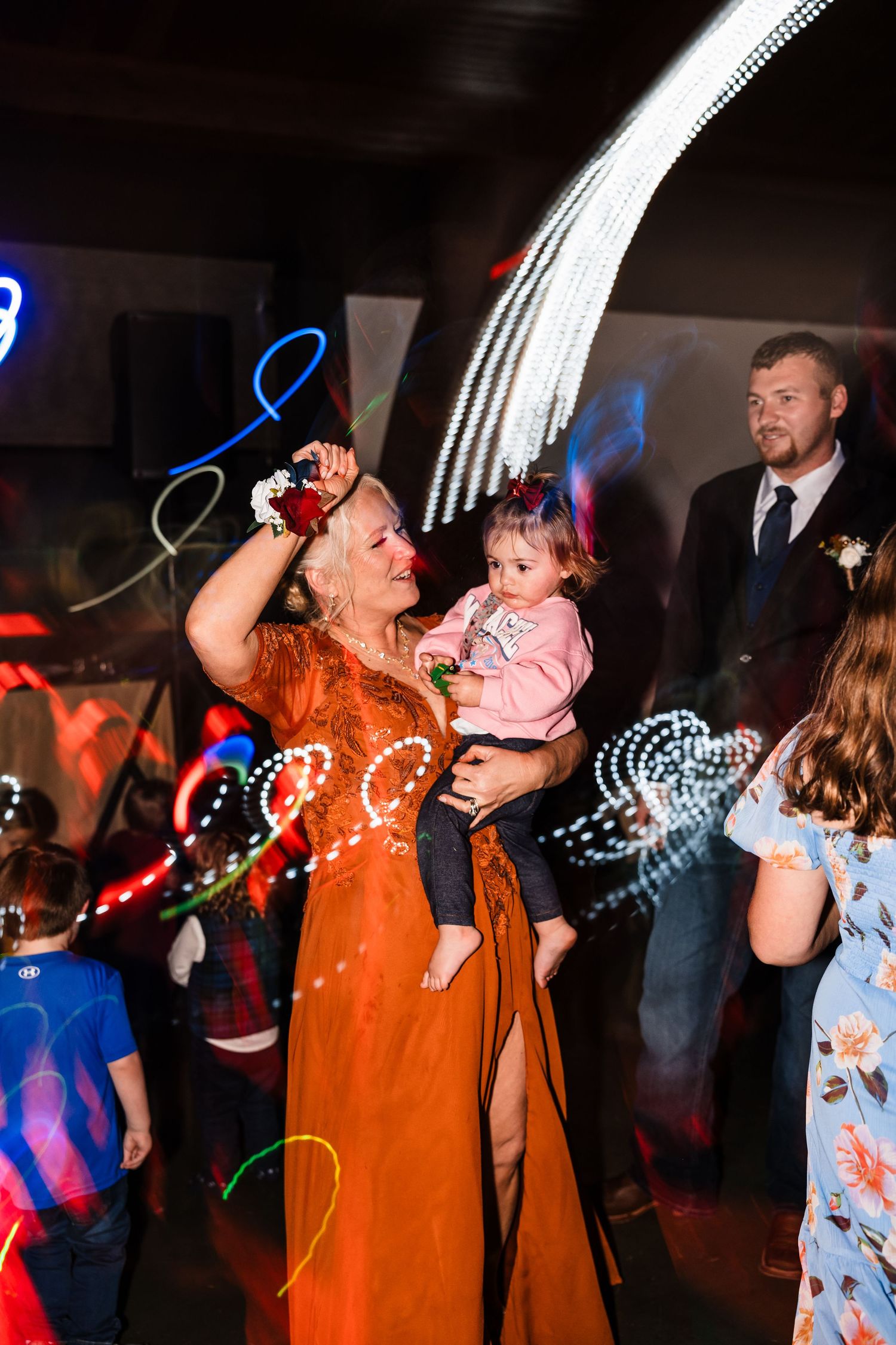 Dancing celebration at wedding reception with colorful light trails and festive atmosphere.