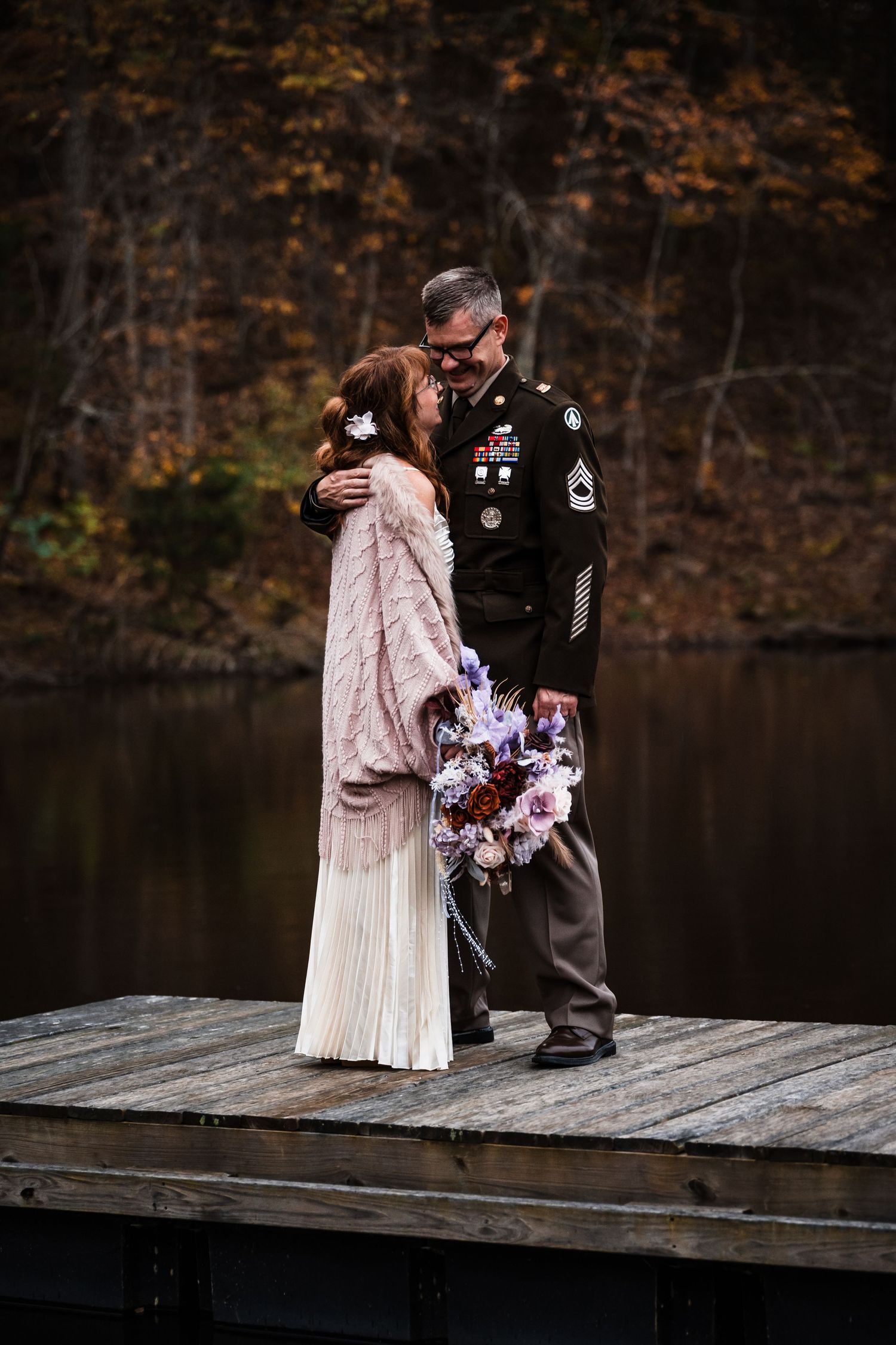 Intimate wedding ceremony moments captured on a wooden dock by a serene lake in autumn.