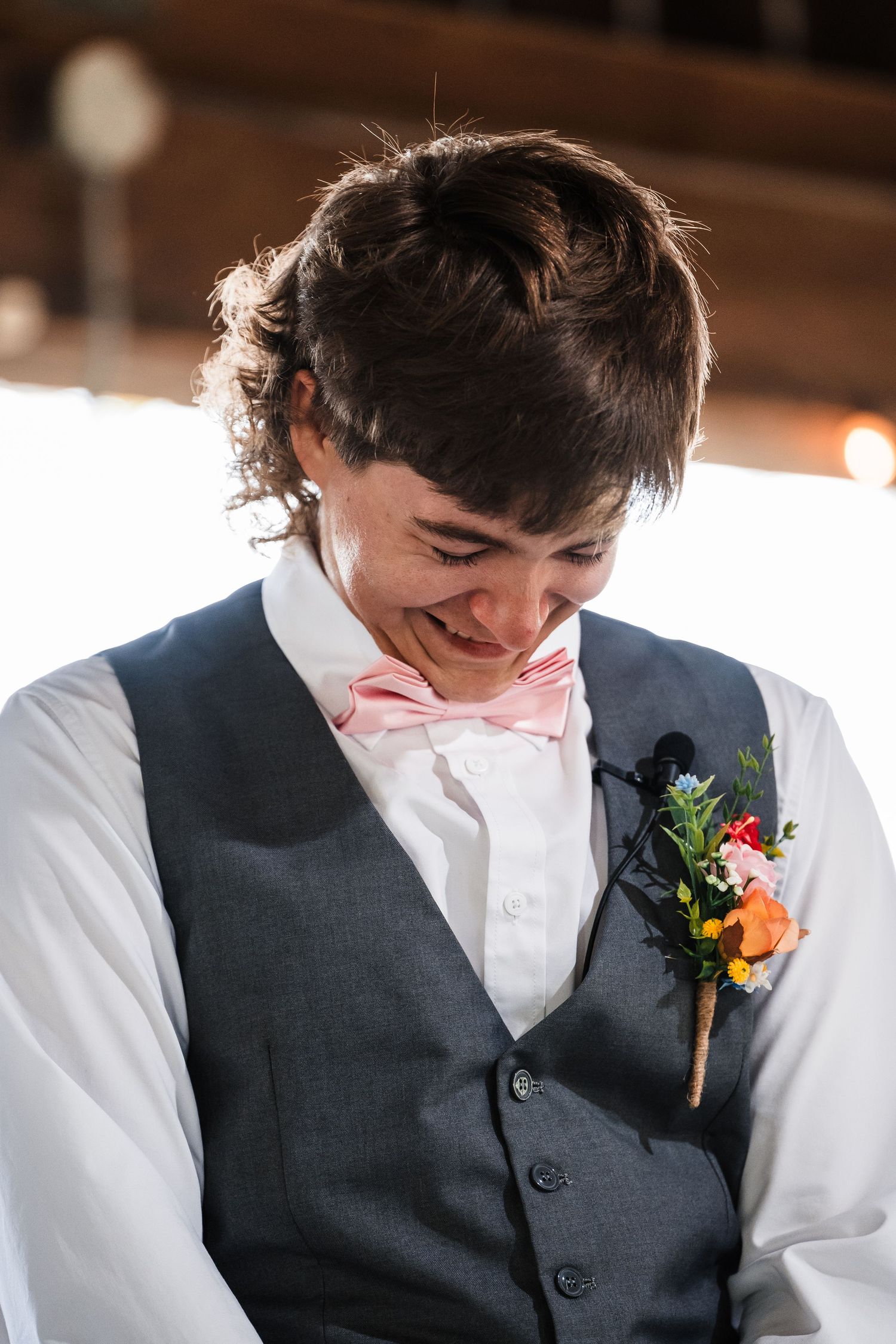 Close up of groom smiling in grey vest and pink bowtie with floral boutonniere.