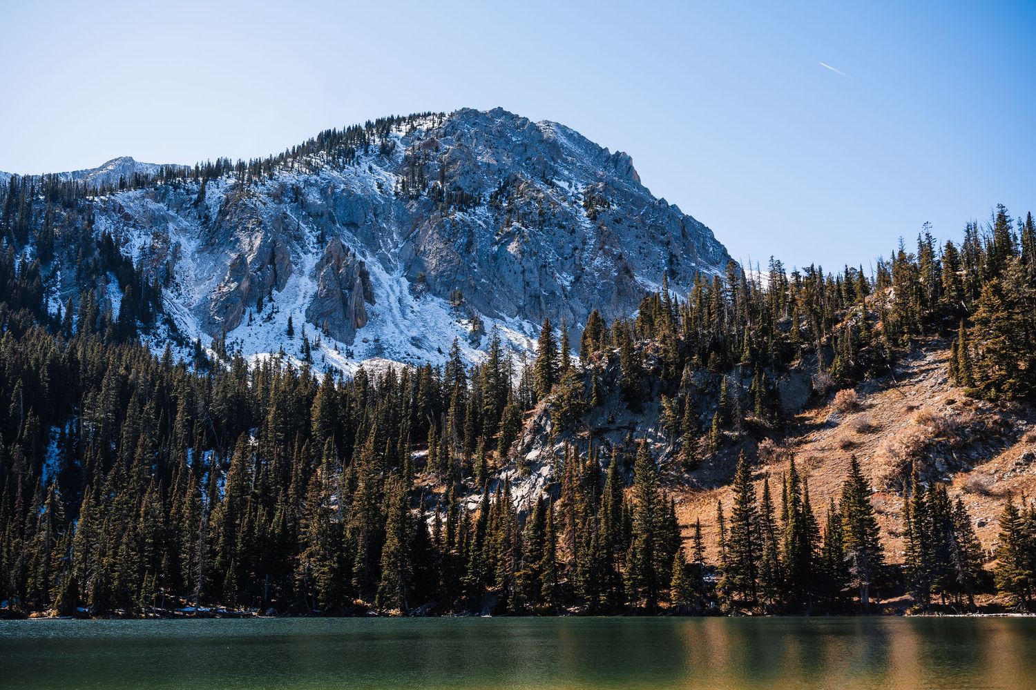 Snow-capped mountain peaks rise above evergreen forests along a scenic alpine lake in winter.
