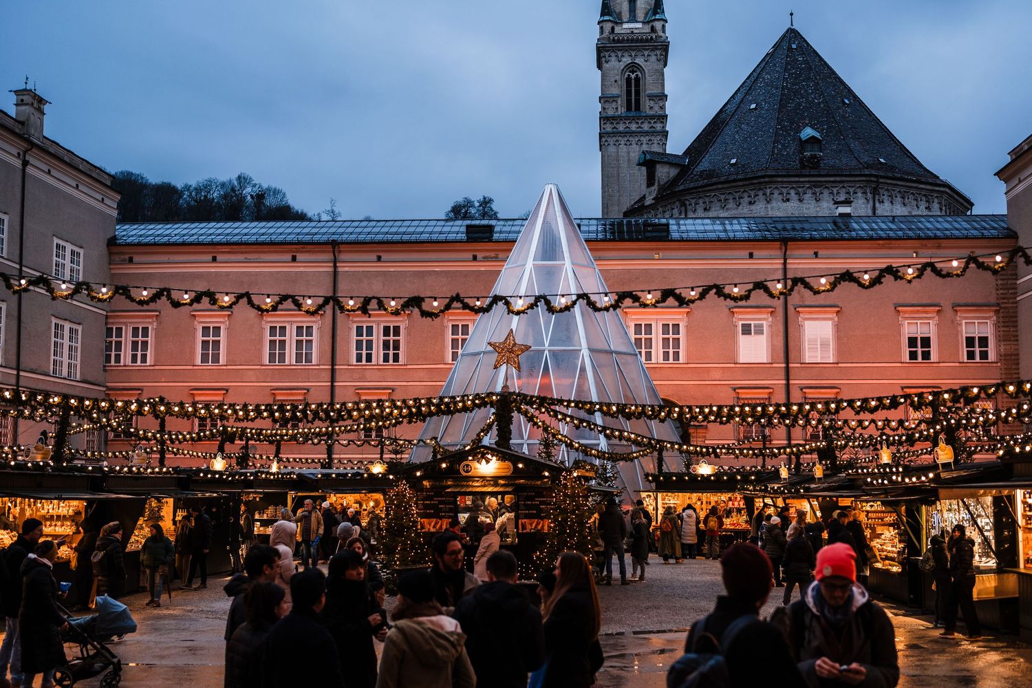 Evening cityscape with festive string lights illuminating historic buildings at dusk.