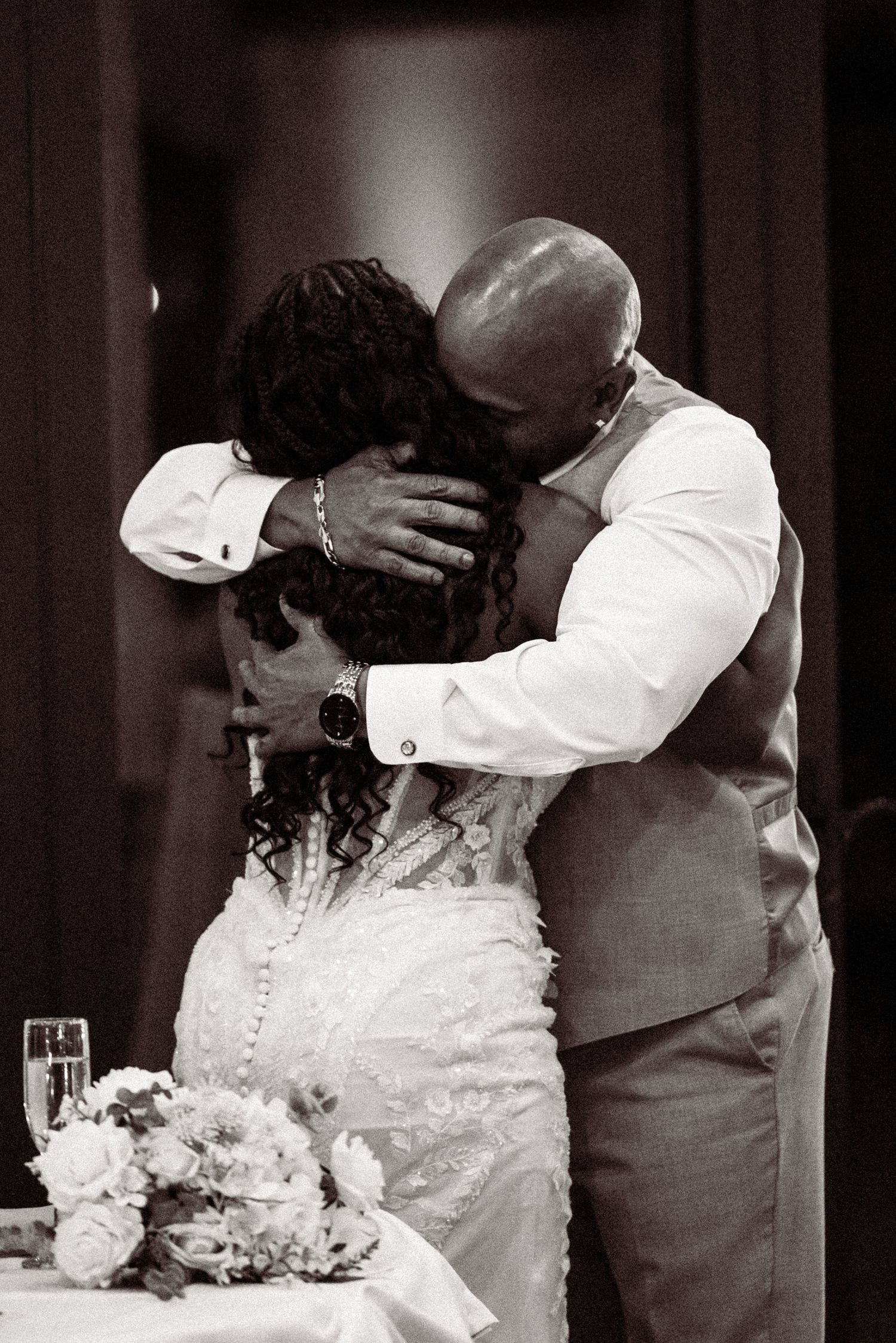 Emotional black and white photo of groom embracing bride tenderly at wedding reception table.