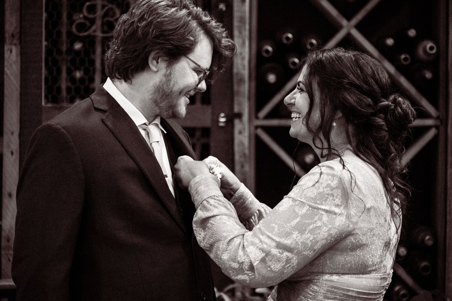 Black and white photo of a joyful couple sharing a tender moment, bride adjusting grooms tie, laughing together.