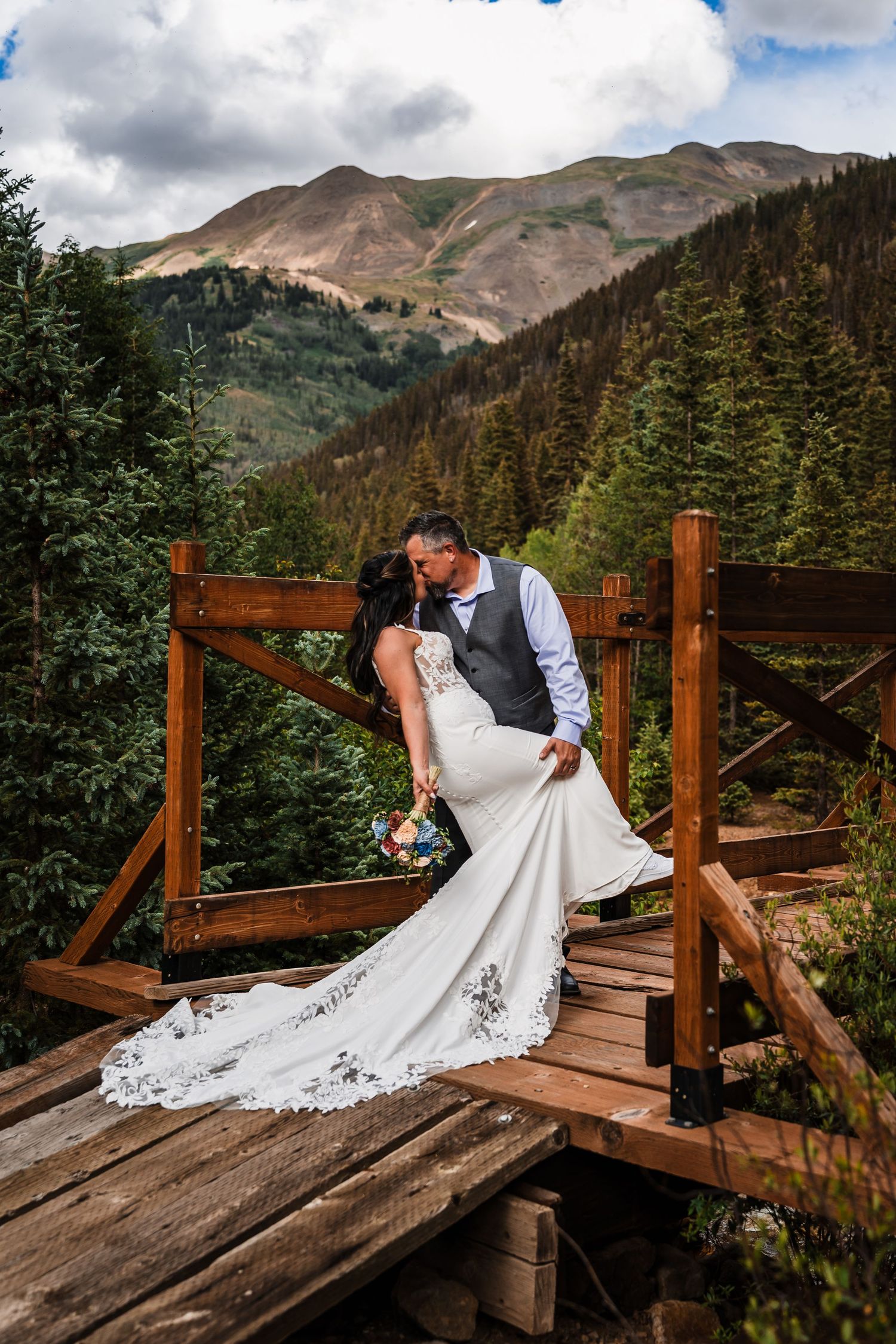 Bride and groom sharing a kiss on a wooden bridge surrounded by Colorado mountain forest.