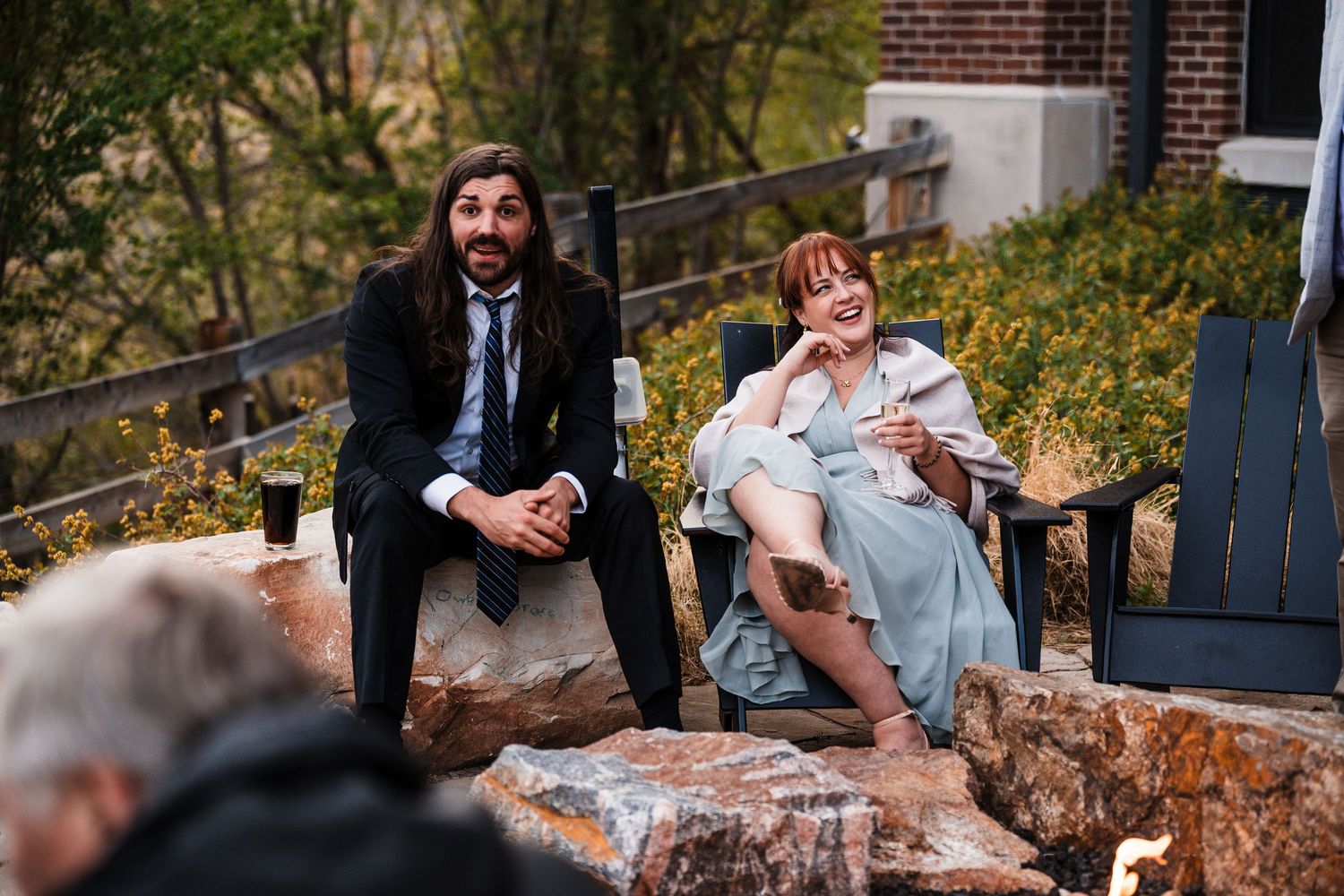 Man and woman relax on stone seating outdoors at a wedding reception gathering.