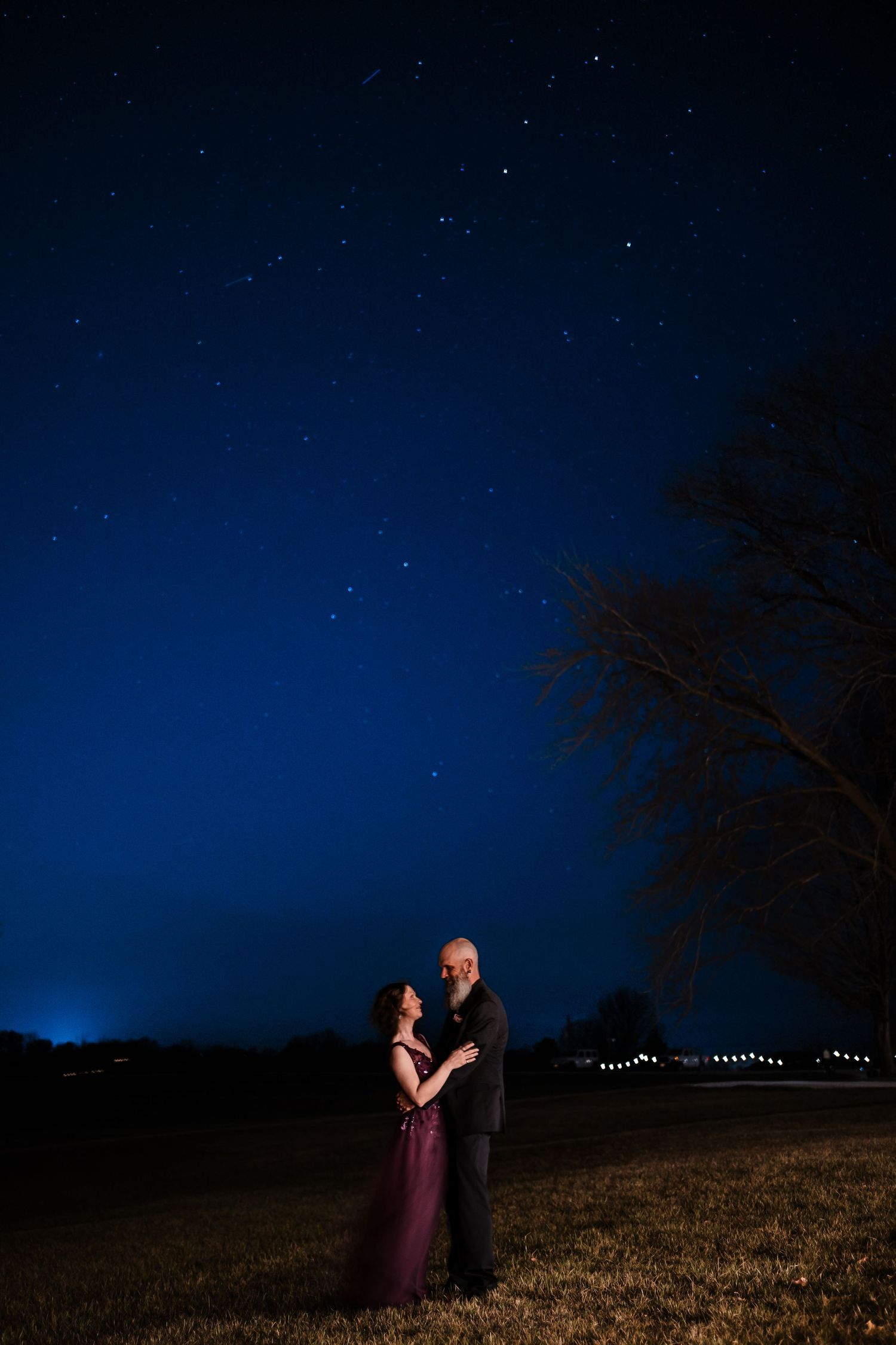 Romantic couple embraces under a stunning starry night sky outdoors in formal wedding attire.