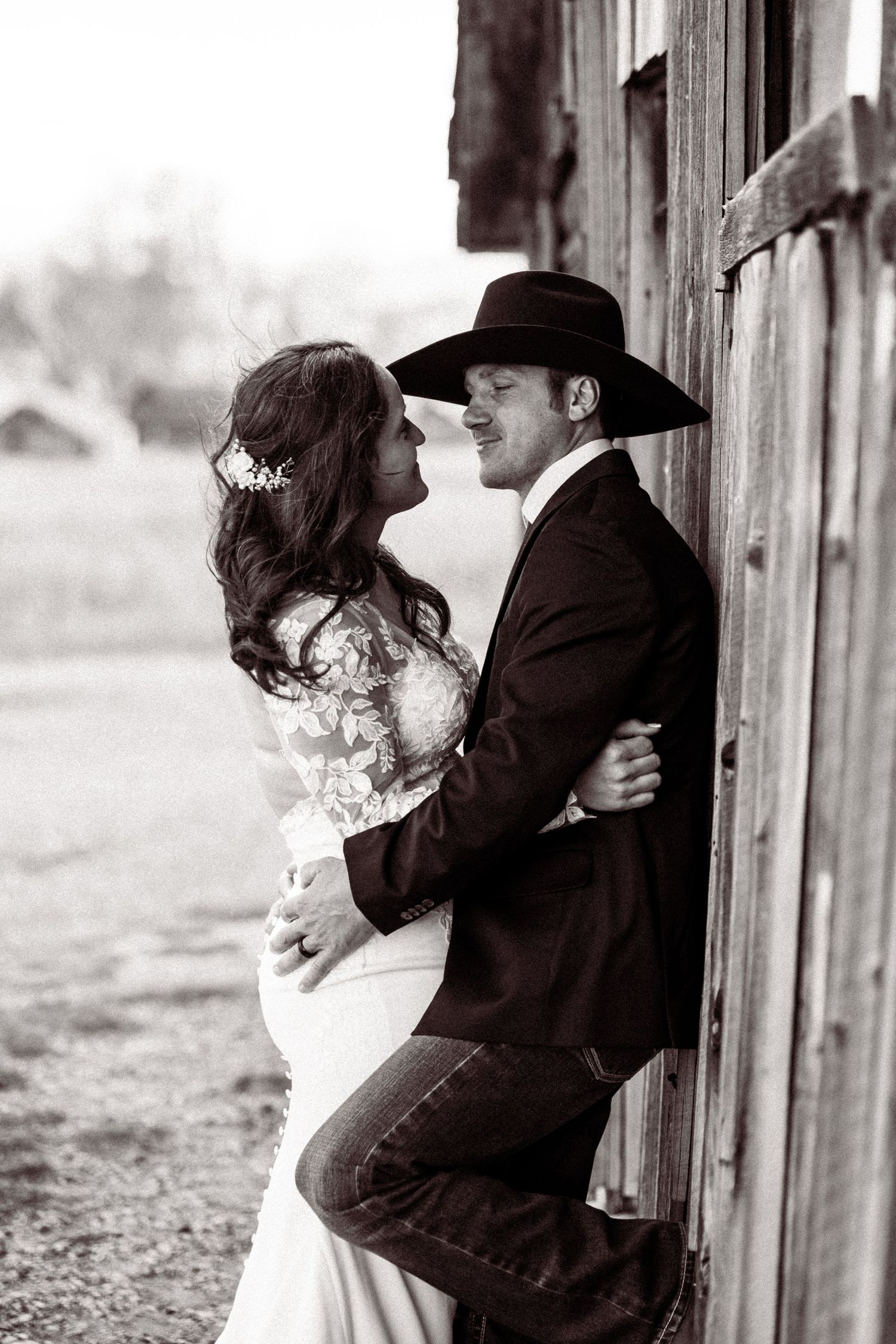 Black and white wedding portraits capturing tender moments between a couple against weathered wood siding.