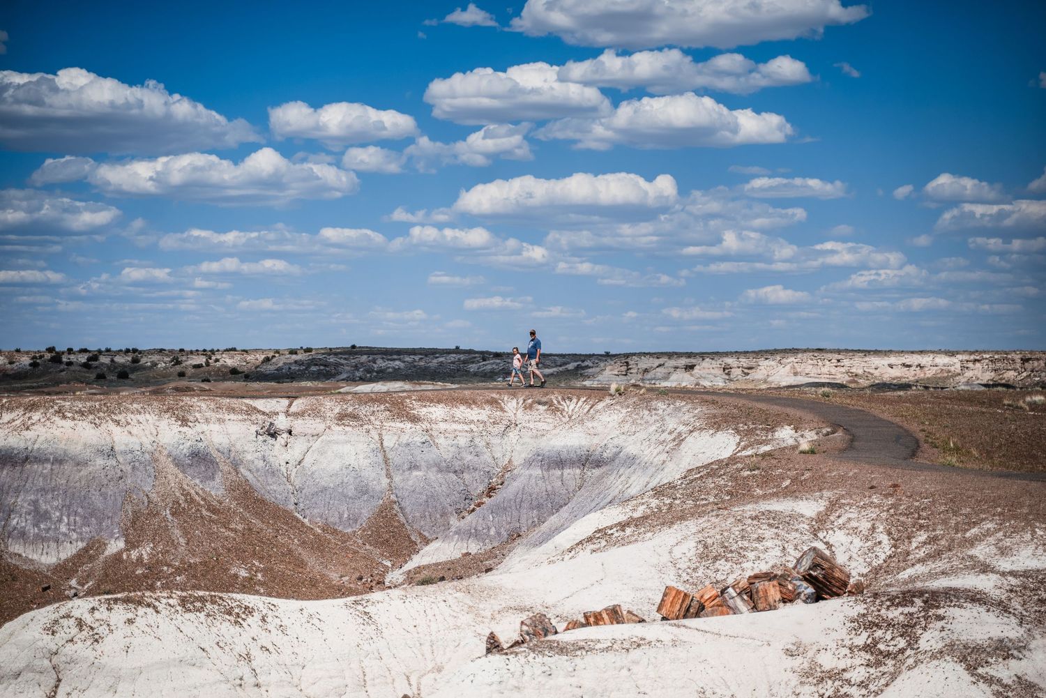 Aerial view of a white clay quarry with curved paths and industrial equipment under puffy clouds in a blue sky.