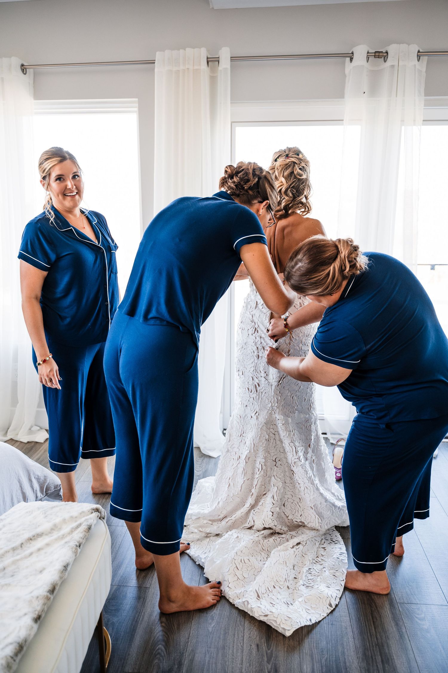 A sequence showing bridesmaids in navy dresses helping with the bride's wedding gown details.