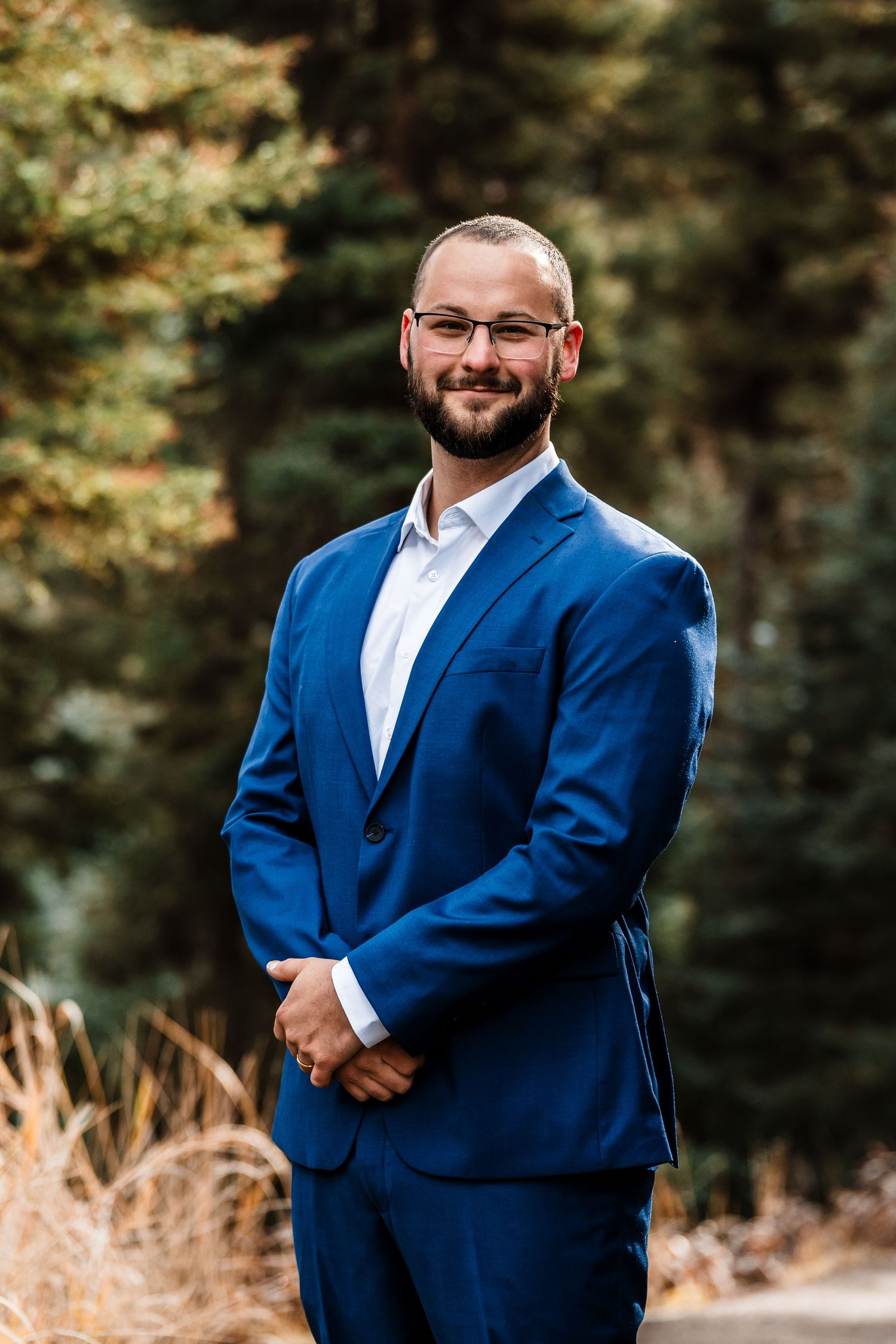 A groom in a royal blue suit poses for portraits in an outdoor setting with natural lighting.