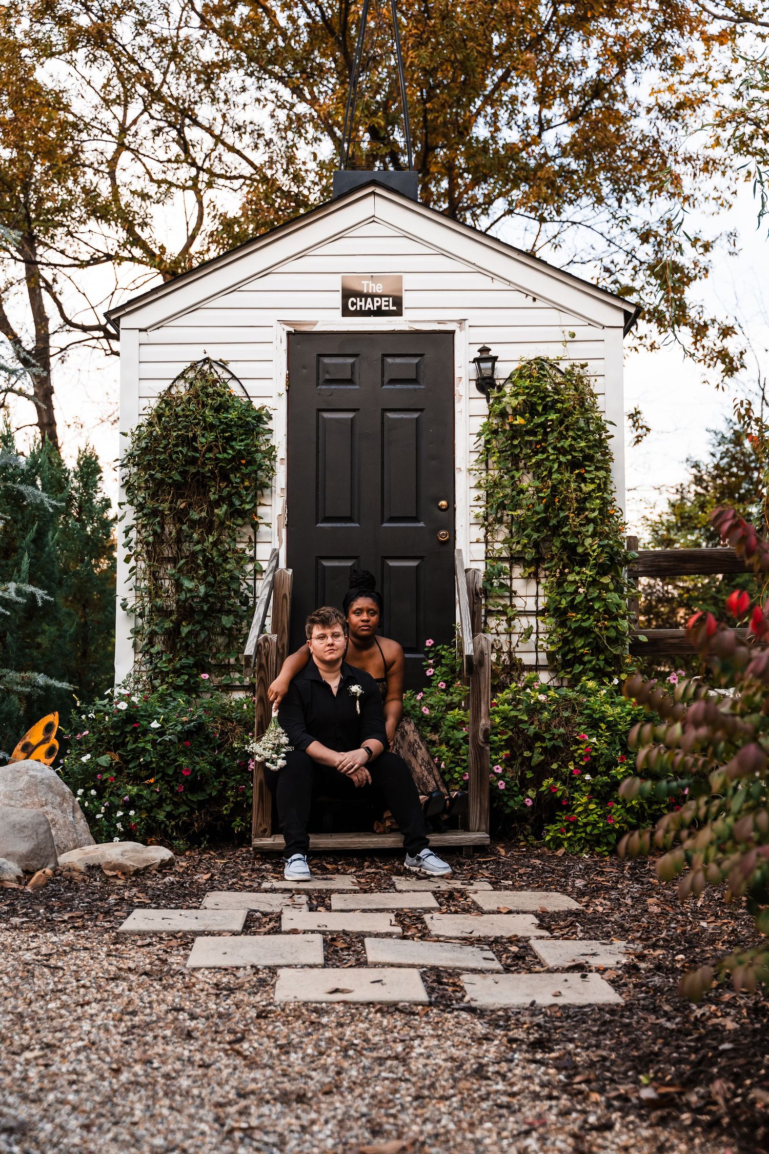 A charming white chapel entrance with black door and climbing vines on autumn day.