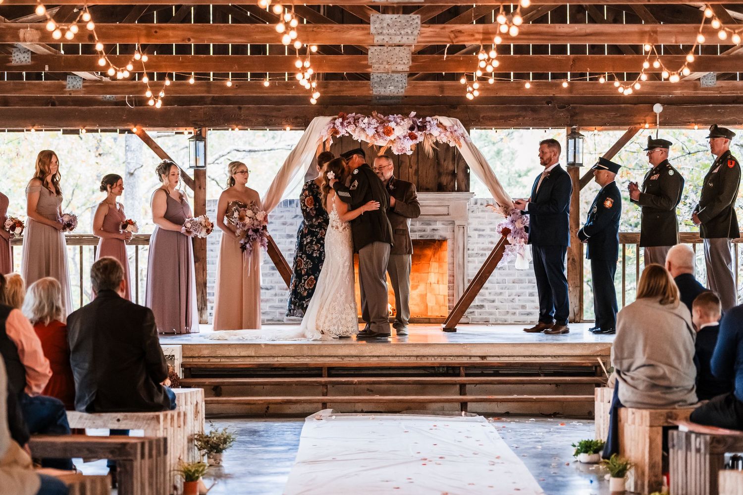 Indoor wedding ceremony with string lights and wooden beams as guests watch the couple exchange vows.