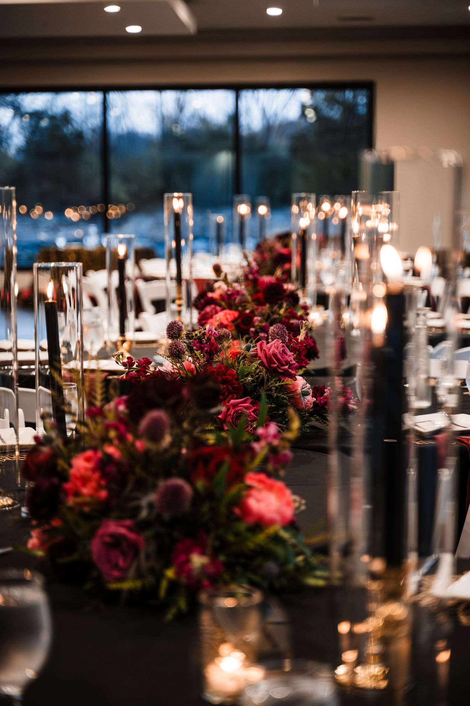 Elegant reception tables decorated with red floral centerpieces and glowing candles.