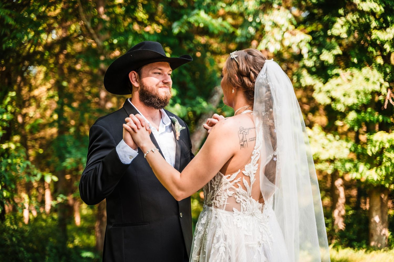 A joyful couple in wedding attire share a romantic dance moment outdoors surrounded by green foliage.
