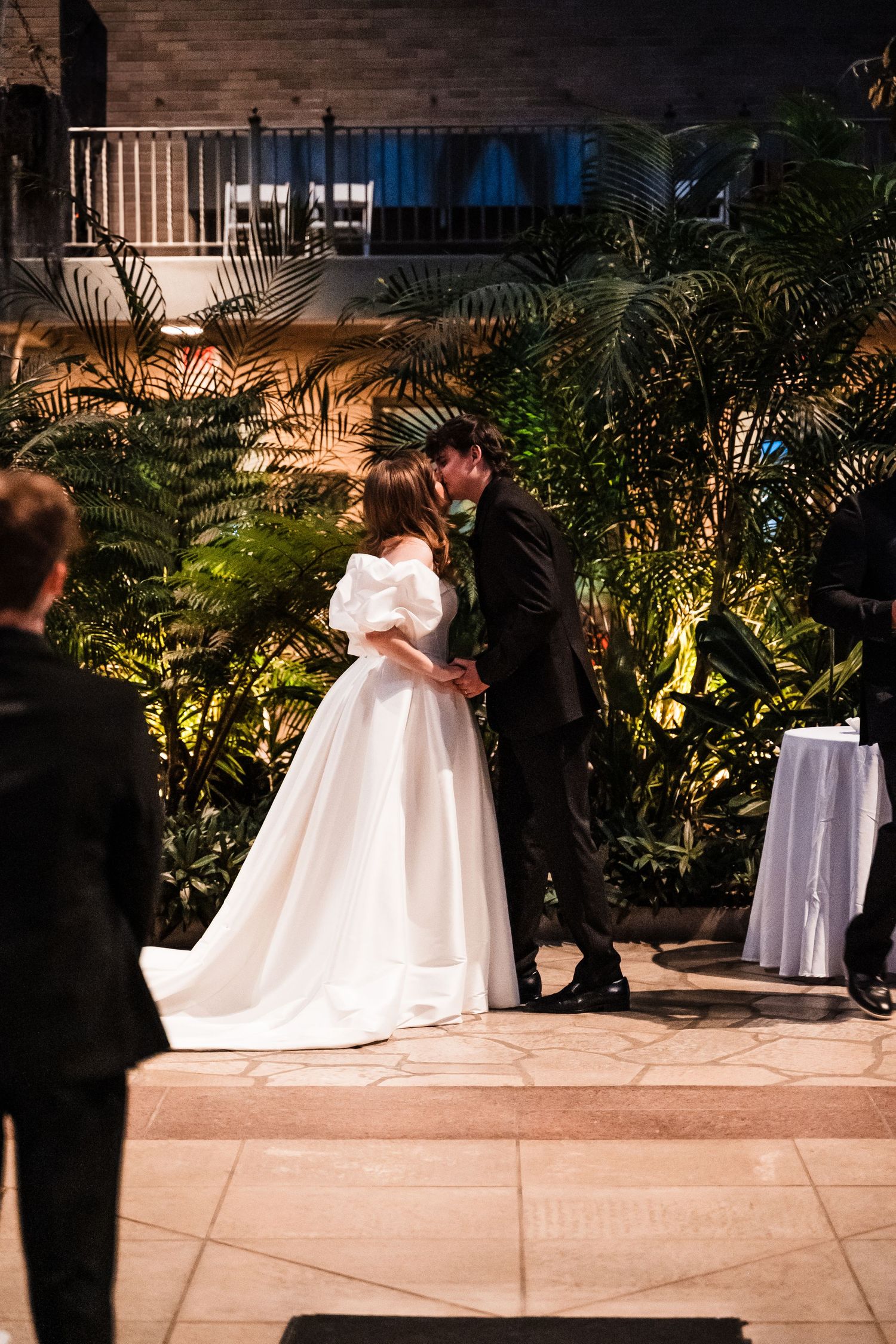 Couple sharing a romantic moment during their evening wedding ceremony surrounded by tropical plants.