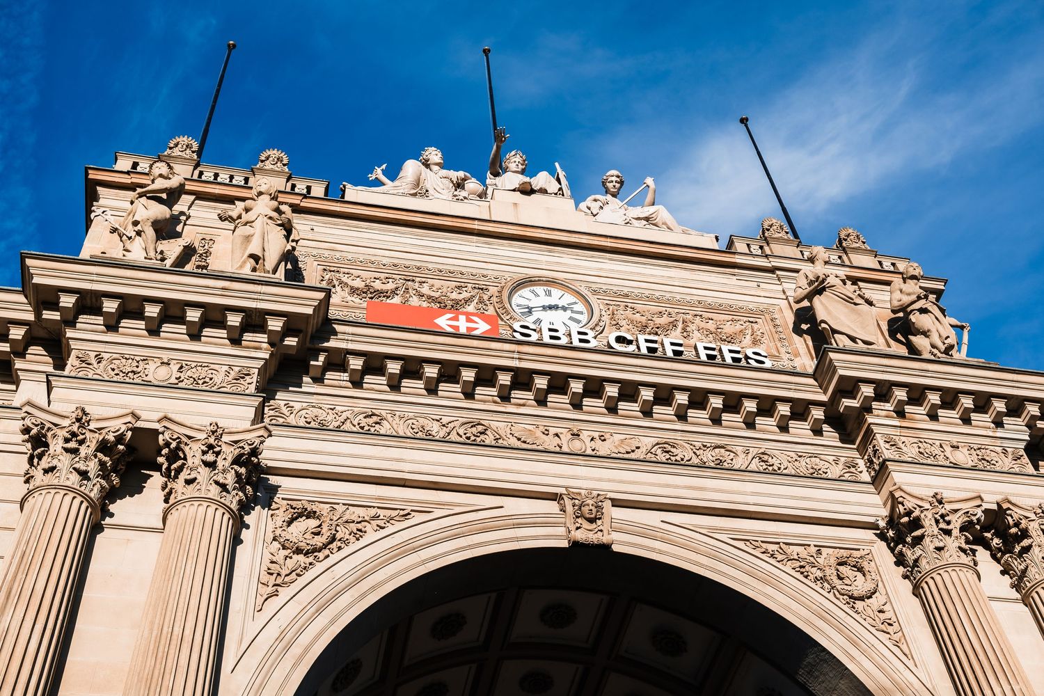 Ornate architectural details of a classical building facade with columns and decorative stonework against a blue sky.